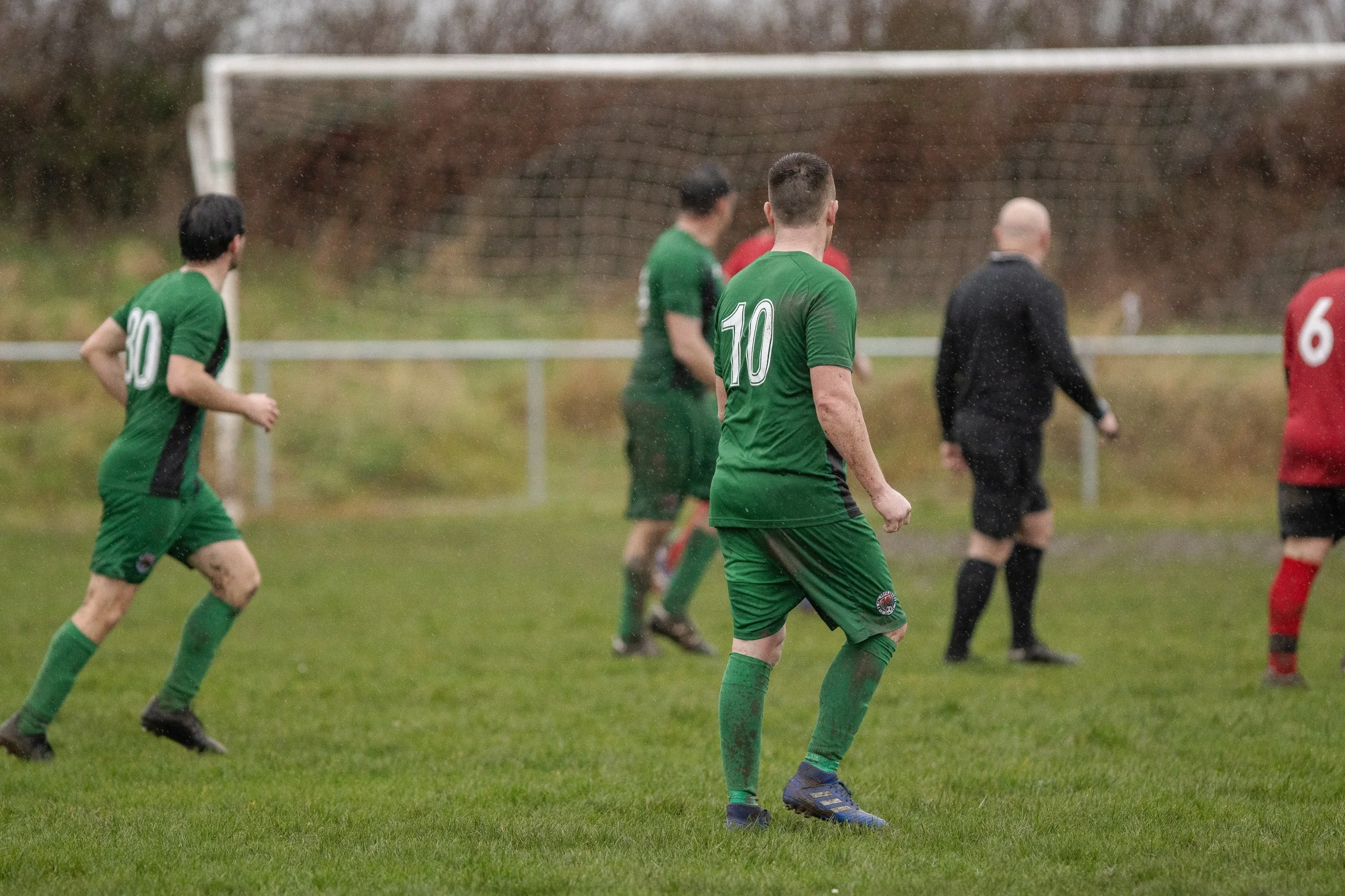 Soccer players in green and red uniforms on a rainy field during a match.