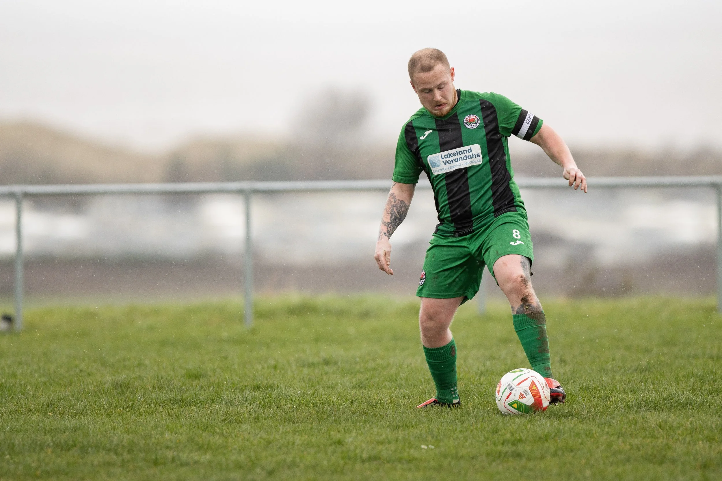 A male soccer player in a green and black uniform kicking a soccer ball on a grassy field.