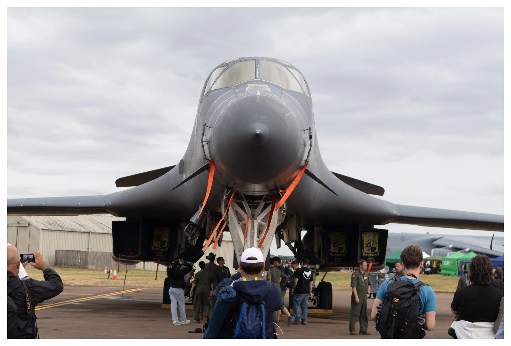 Front view of a military fighter jet on display at an airshow, with people taking photos and observing around it.