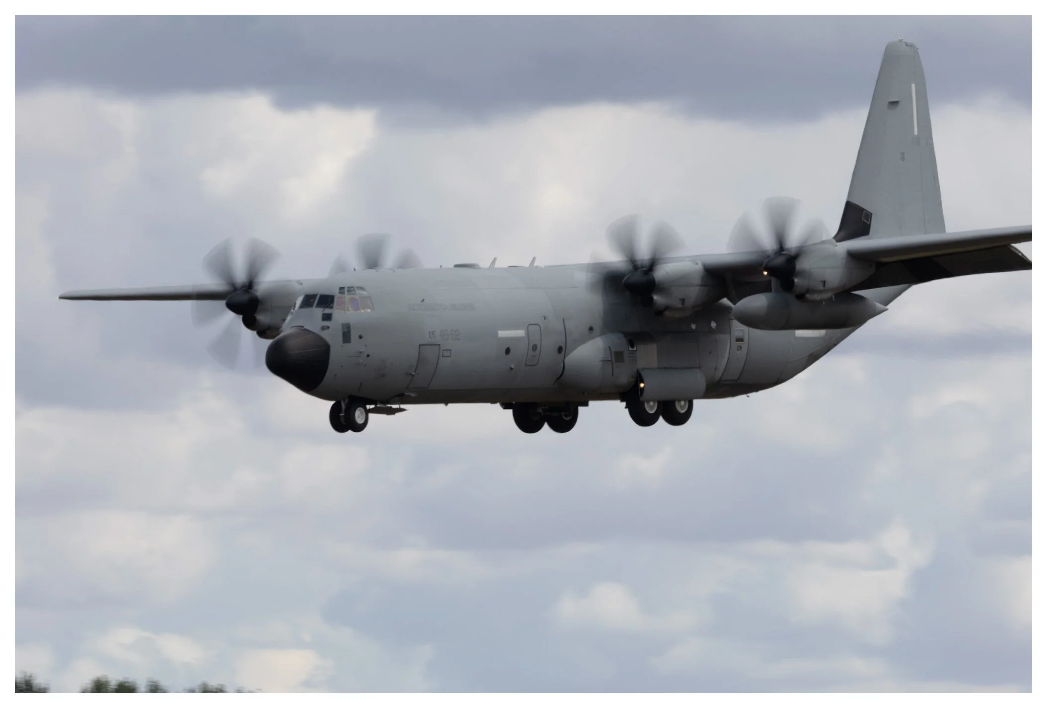 A military gray cargo airplane with four propellers flying in cloudy skies.