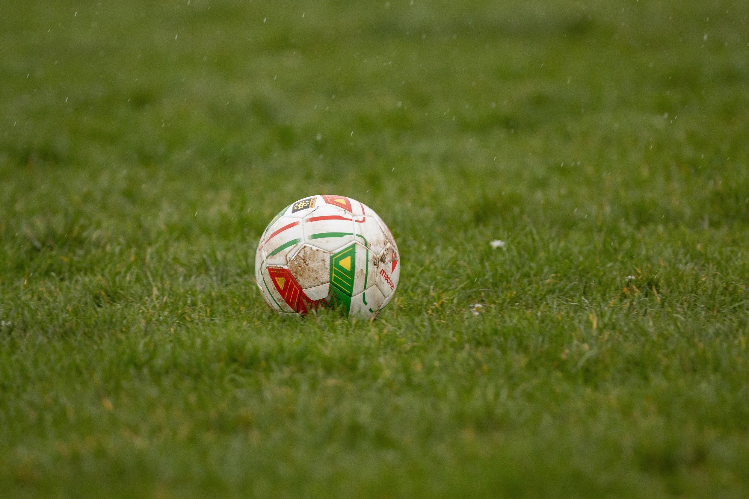 Soccer ball on grass field, with mud stains and dirt on surface.
