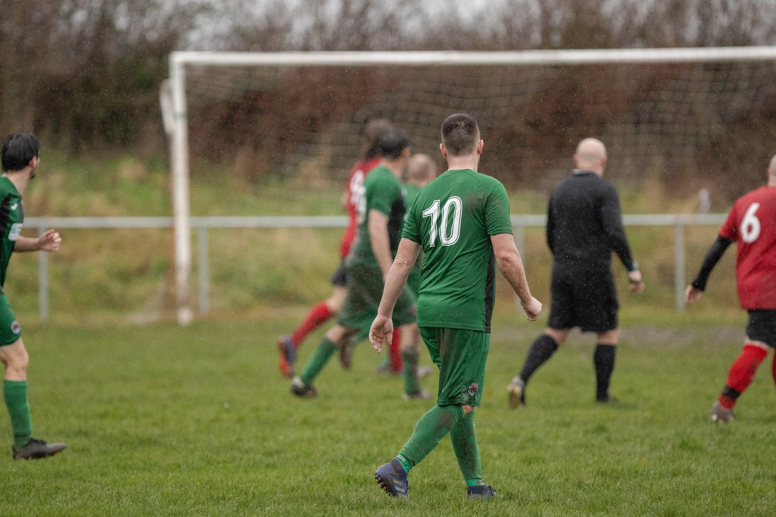 A soccer player in a green uniform with the number 10 on the back on a rainy field during a game, with other players and a referee in the background.