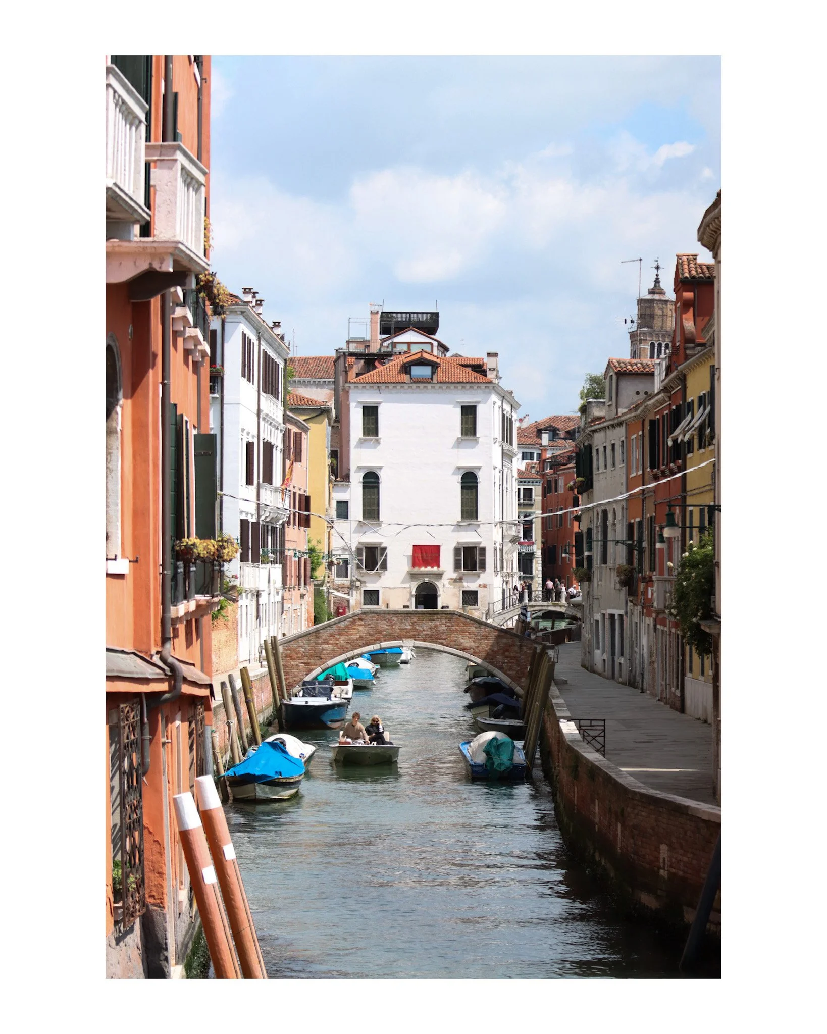 A canal in Venice, Italy, with small boats and colorful historic buildings on either side, under a partly cloudy sky.