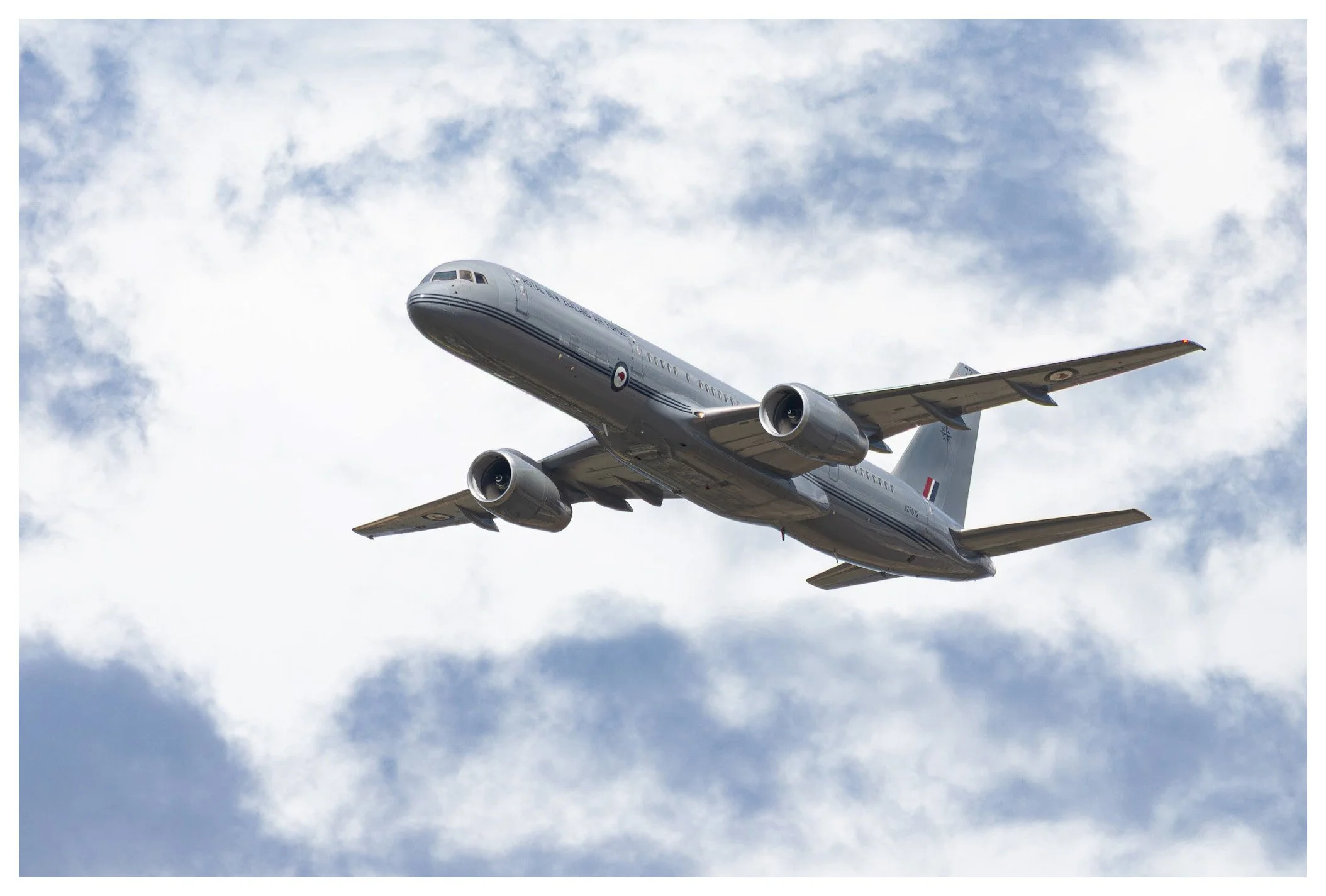 A gray commercial airplane flying through a partly cloudy sky.