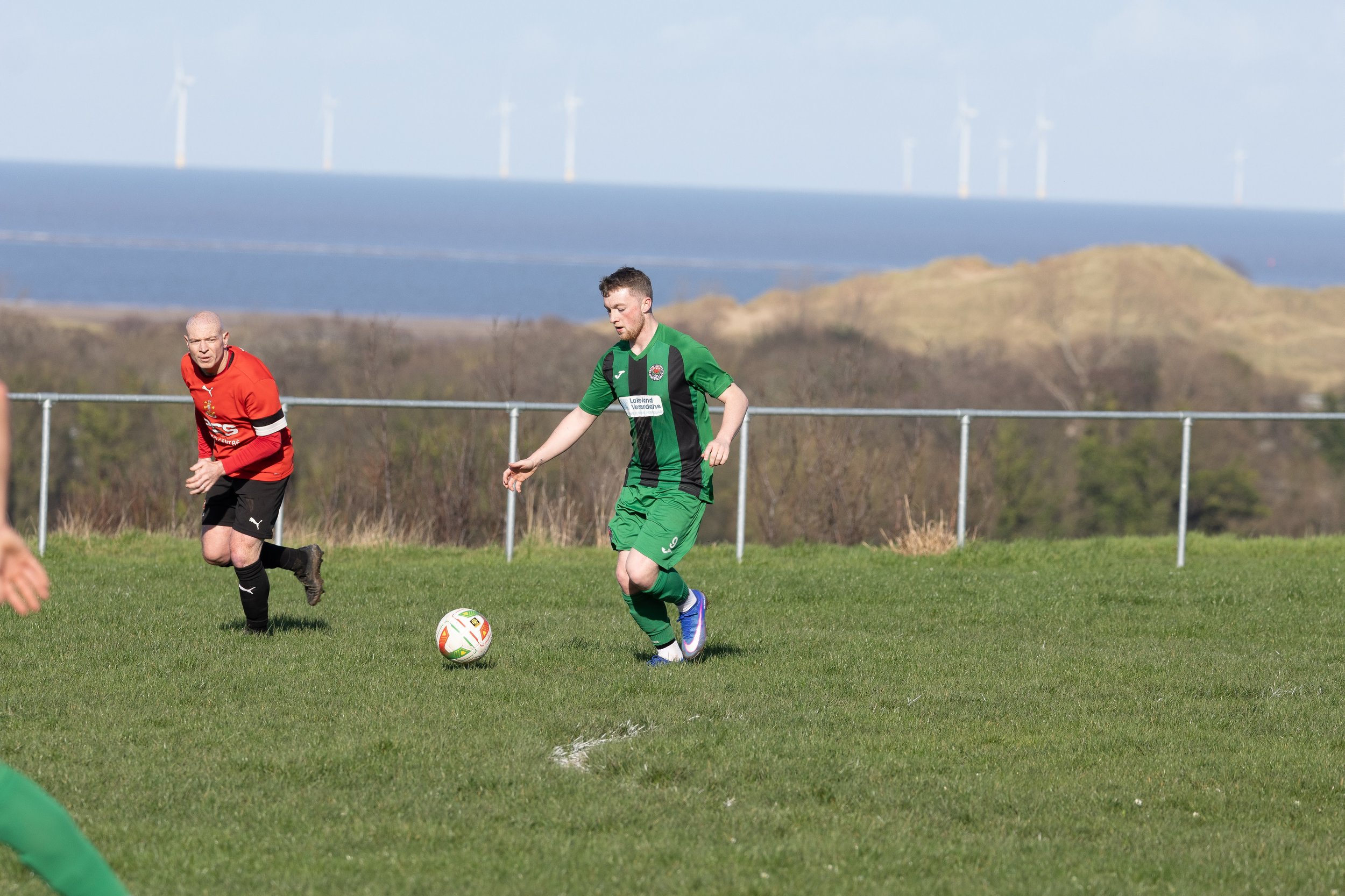 A soccer player in a green and black uniform controlling the ball on a grassy field during a match.