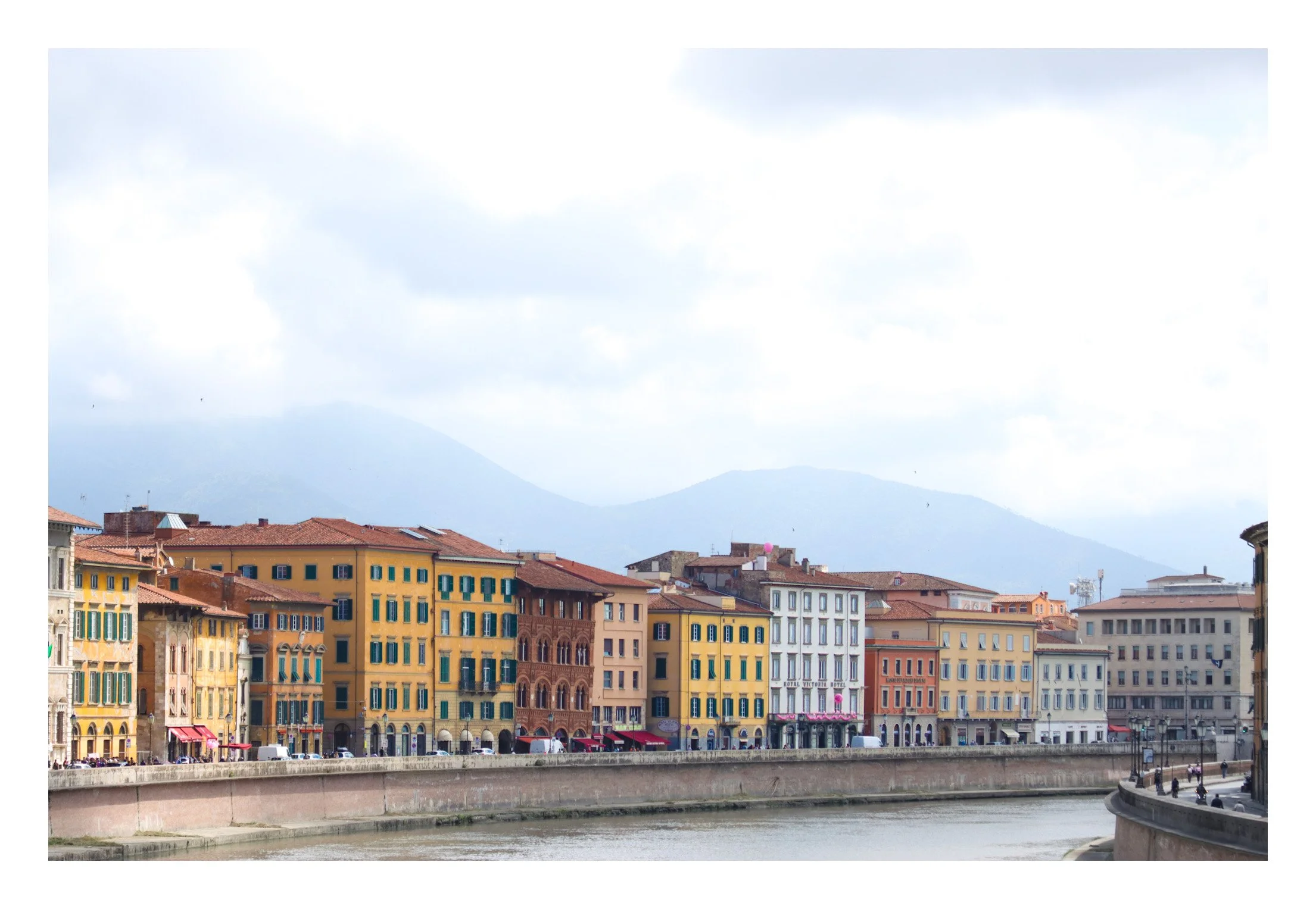 Colorful buildings lining a river with mountains in the background and cloudy sky.