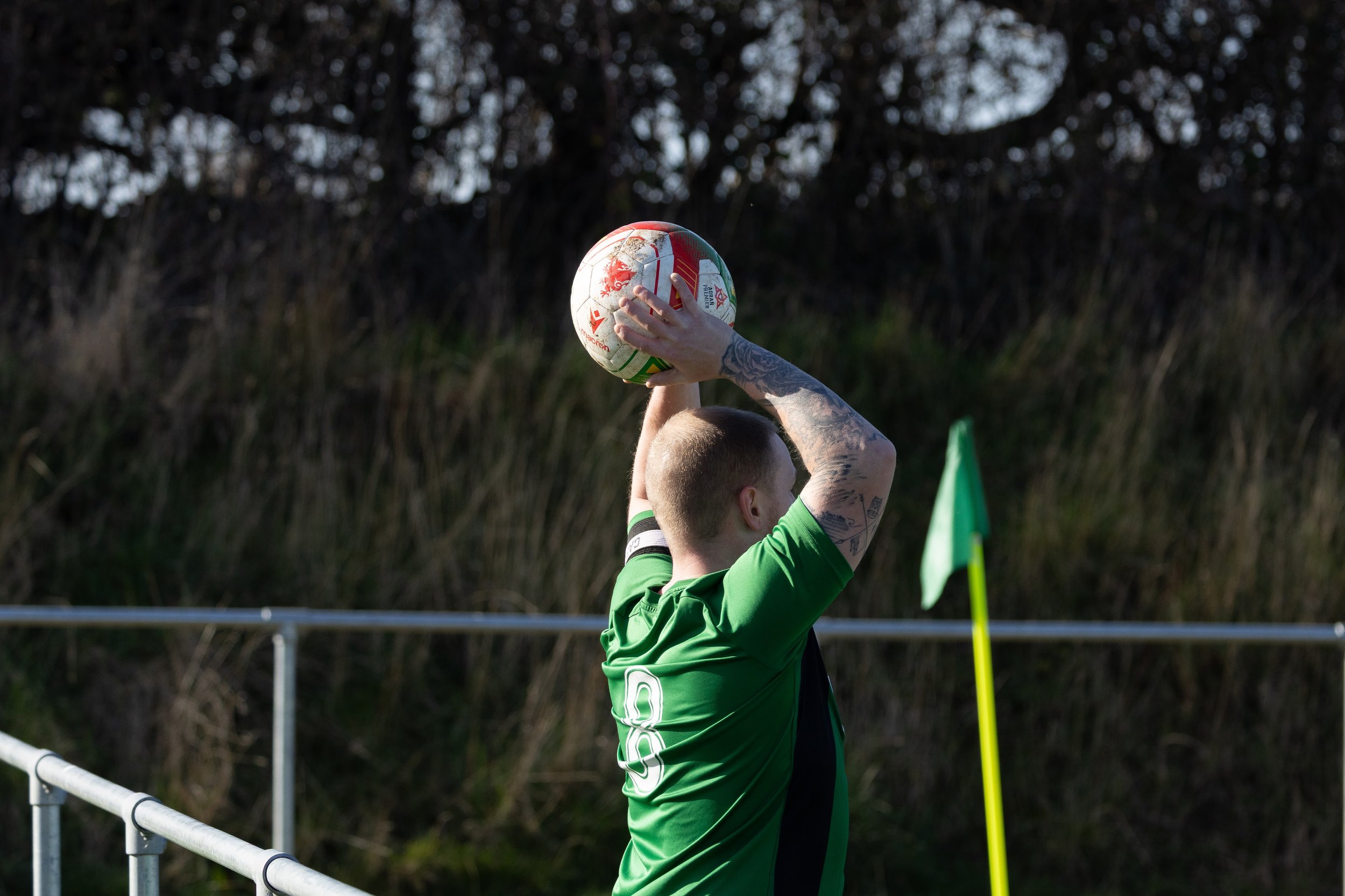 A man wearing a green sports jersey preparing to kick a rugby ball during a game.