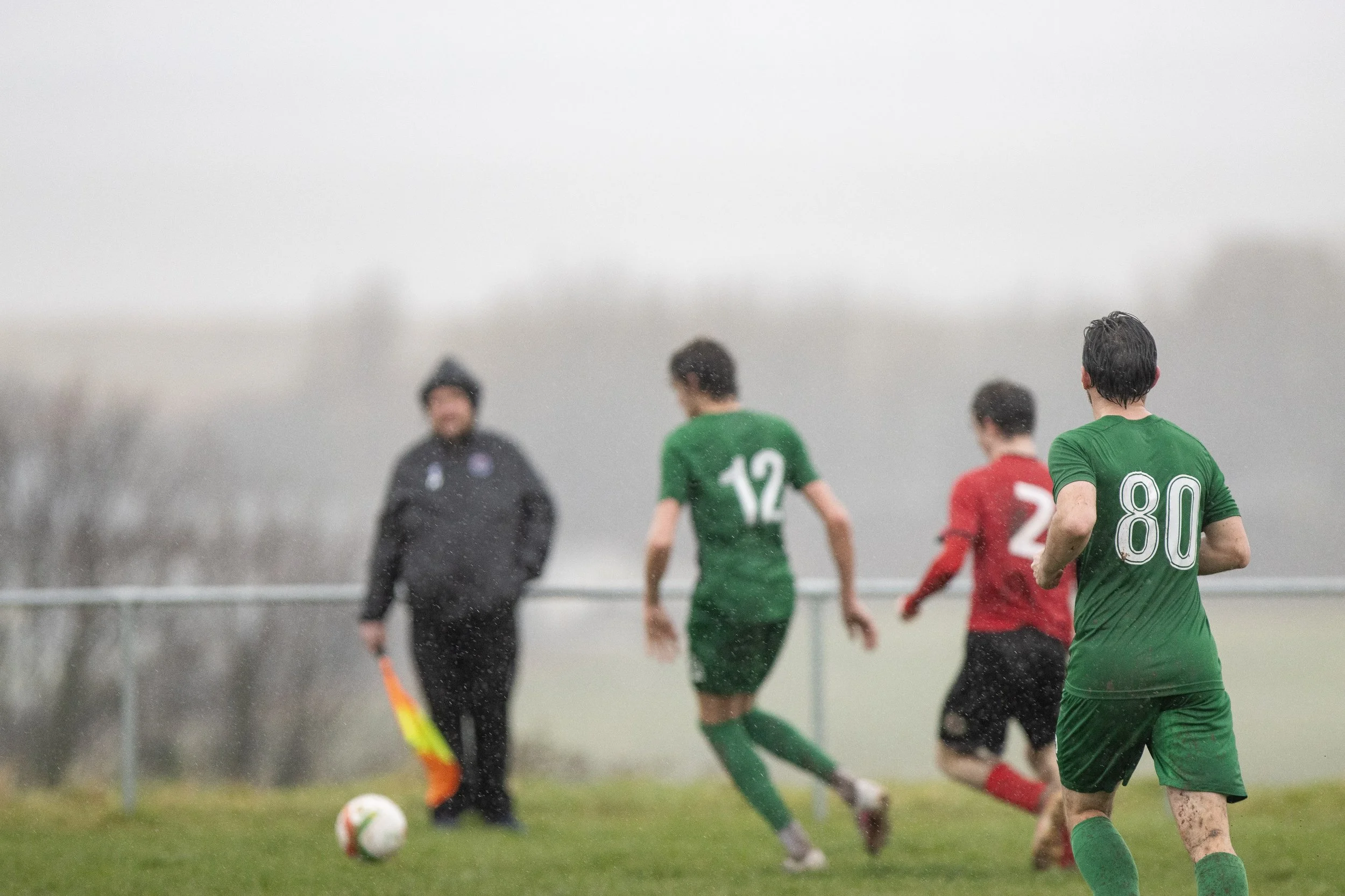 A rainy soccer match with players in green and red jerseys, and an official holding a substitution board.