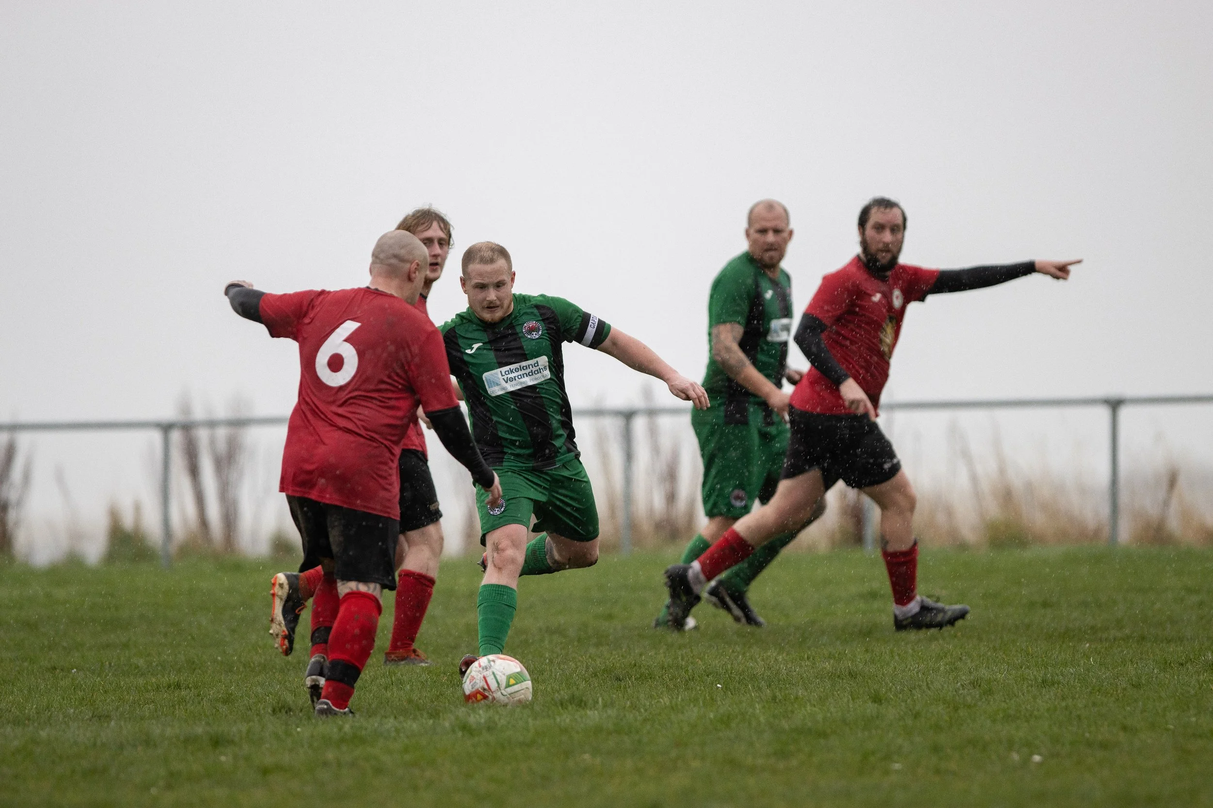 Soccer players in green and red jerseys playing on a wet field during a match.