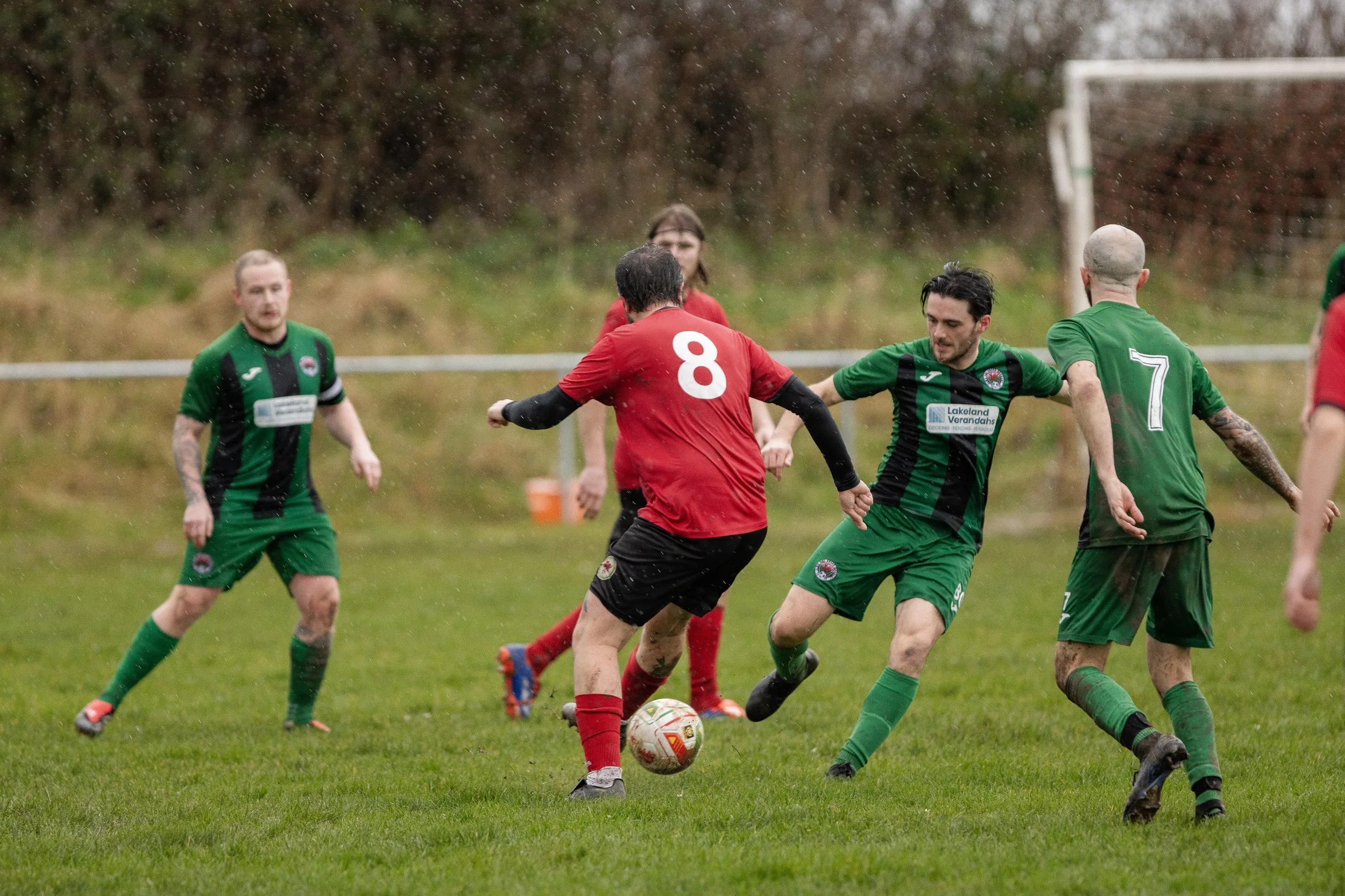 Soccer match with players in red and green uniforms on a rainy field.