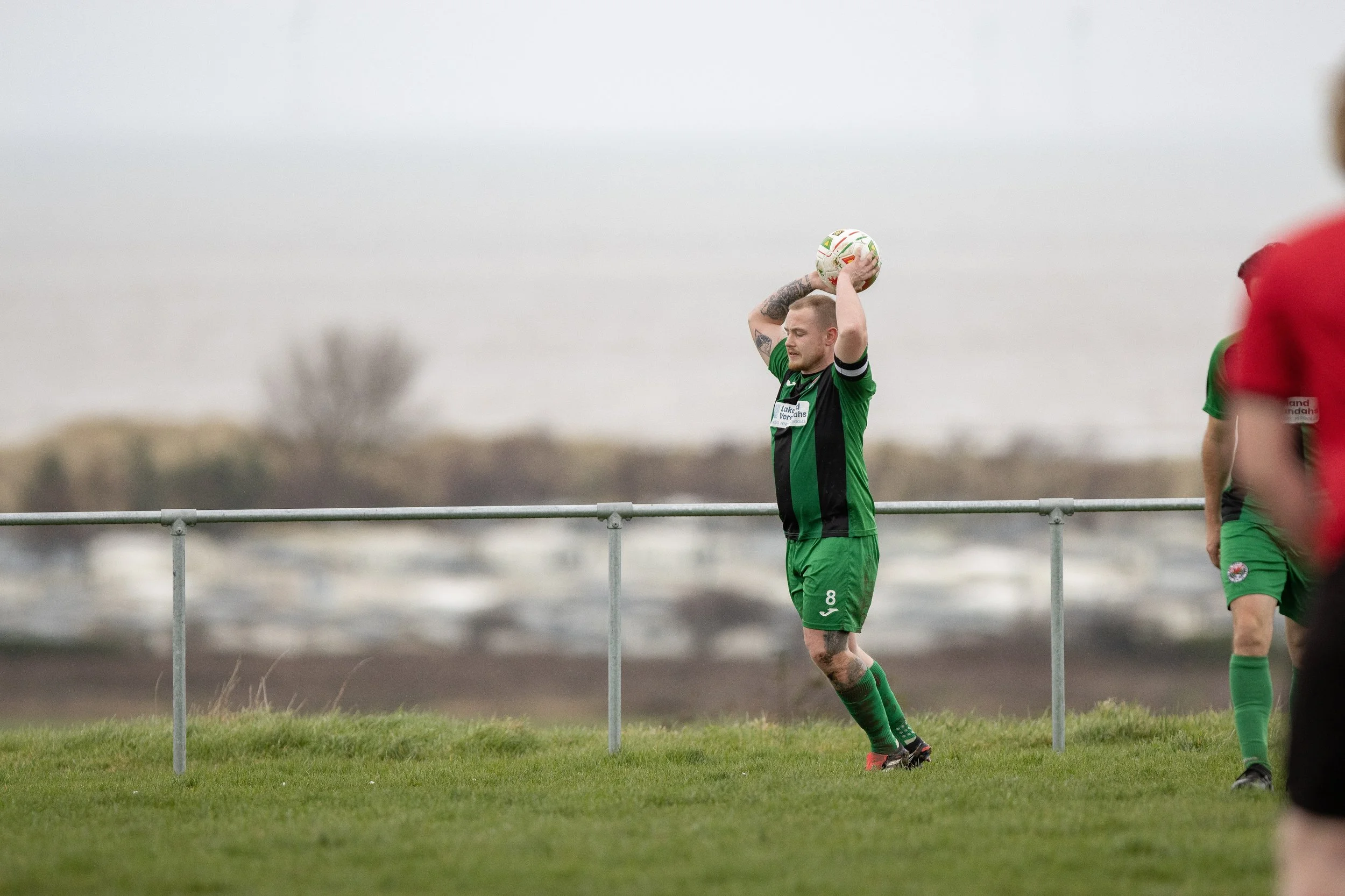 A soccer player in a green and black uniform preparing to throw a soccer ball in a game.