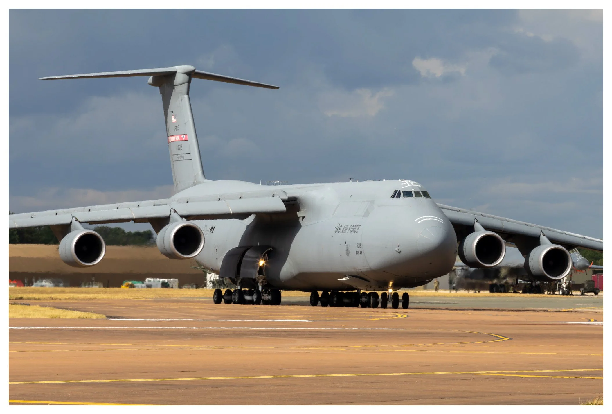 A large military cargo airplane on the runway with four engines, part of the U.S. Air Force, under a cloudy sky.