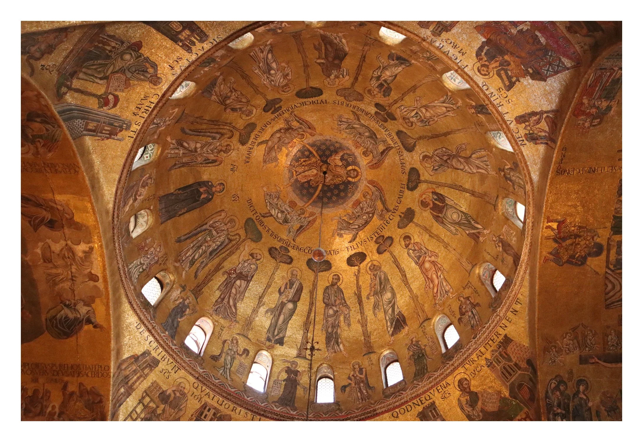 Interior view of a gold mosaic dome featuring religious icons and figures in a circular pattern, with small arched windows around the base.