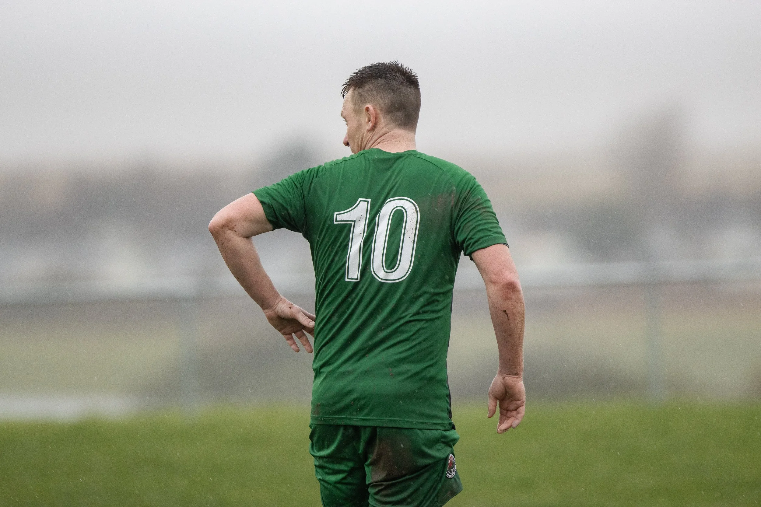 A soccer player wearing a green jersey with the number 10 on the back, standing on a field in rainy weather.