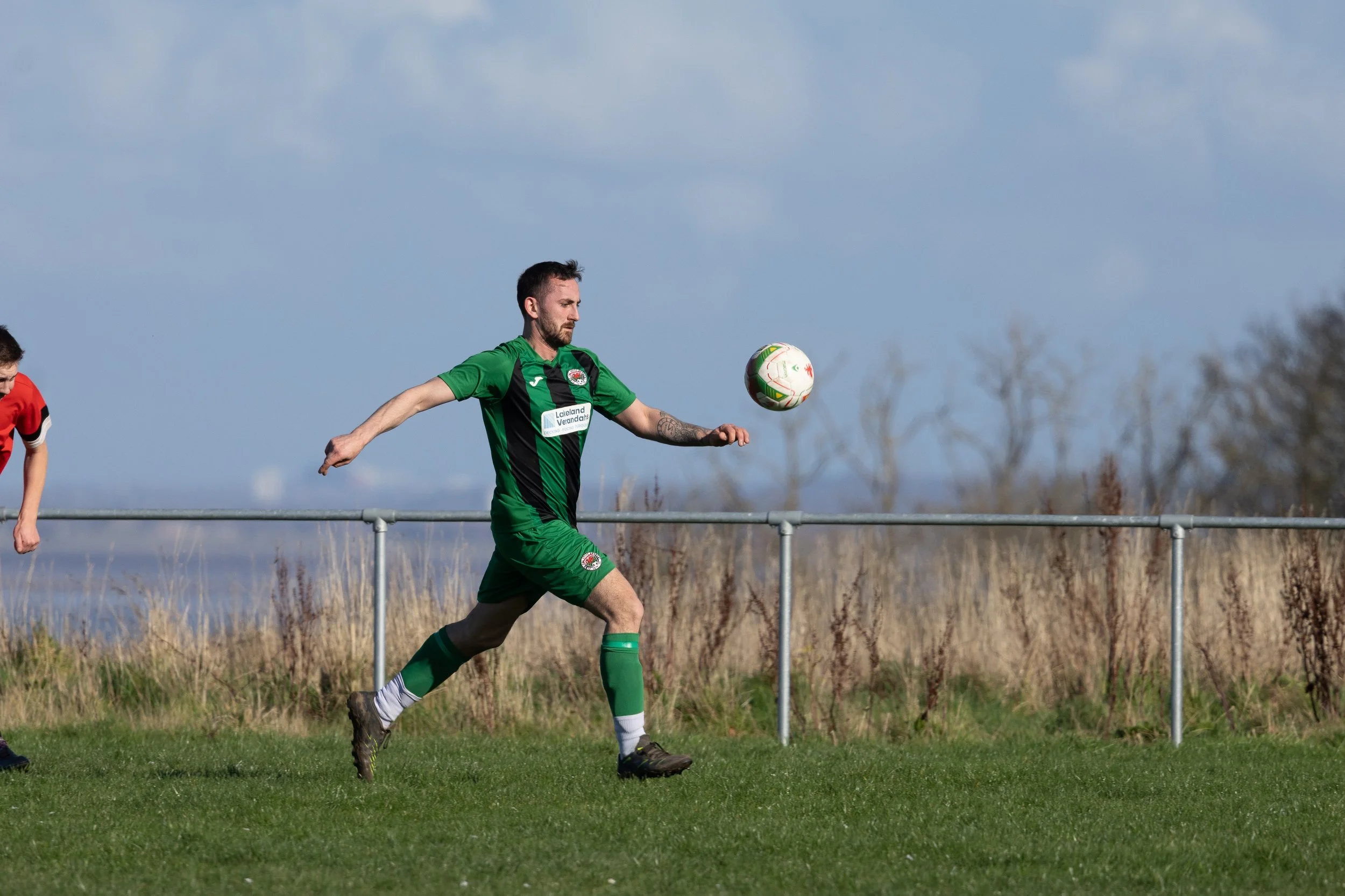 Male soccer player in green and black uniform running and preparing to kick a white soccer ball on a grassy field.