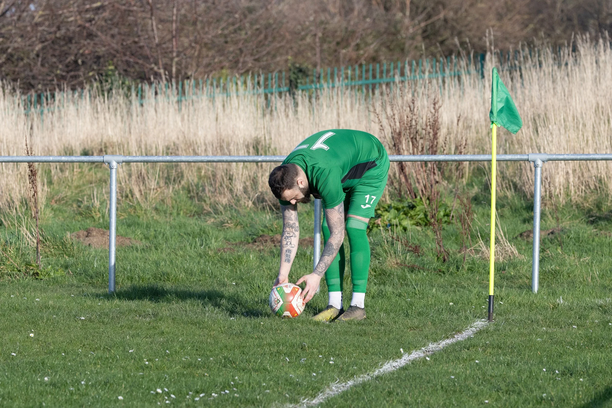 A soccer player in a green uniform placing a soccer ball on the corner kick spot near the corner flag on a grassy field.