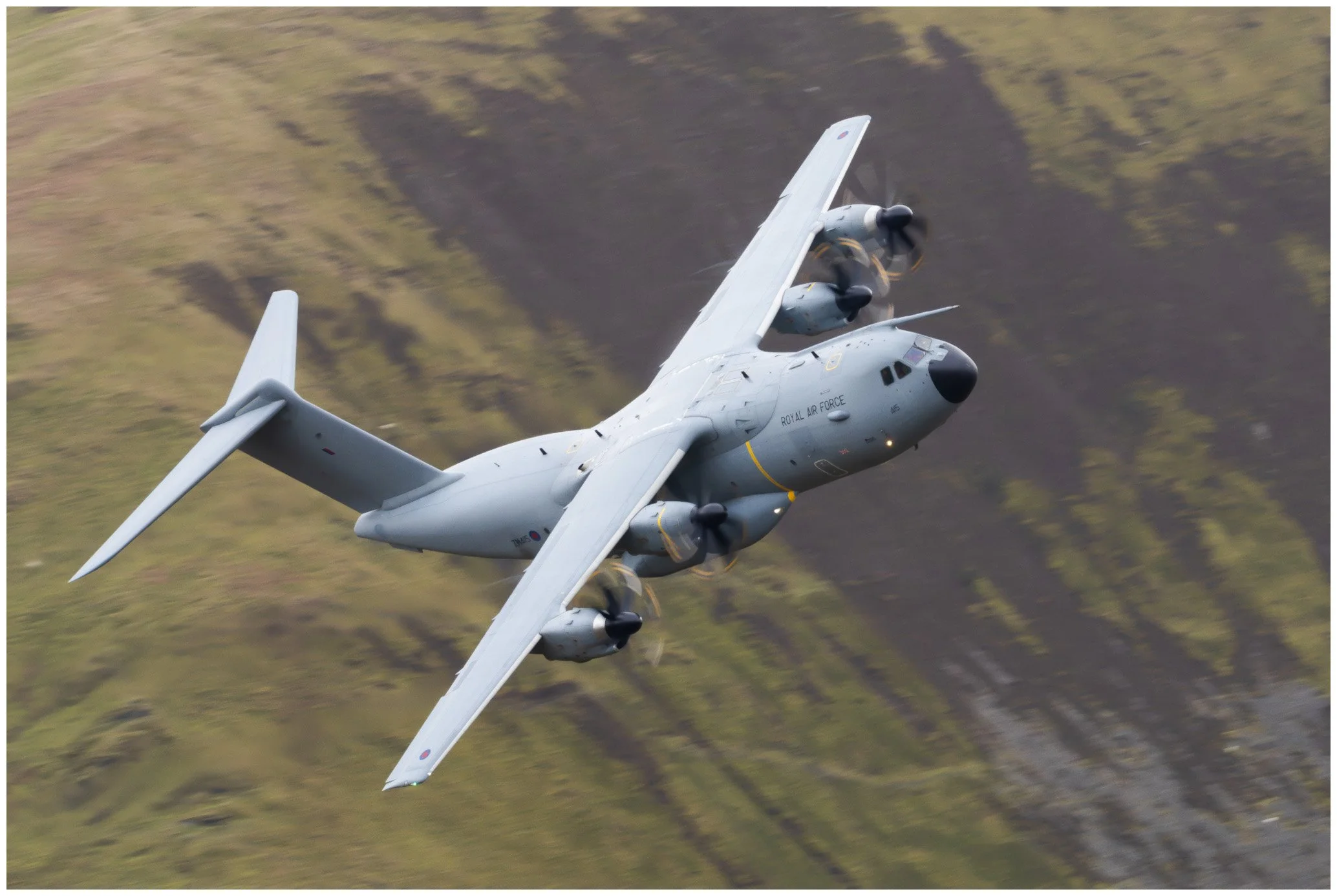 A military aircraft flying through the sky above a grassy landscape.