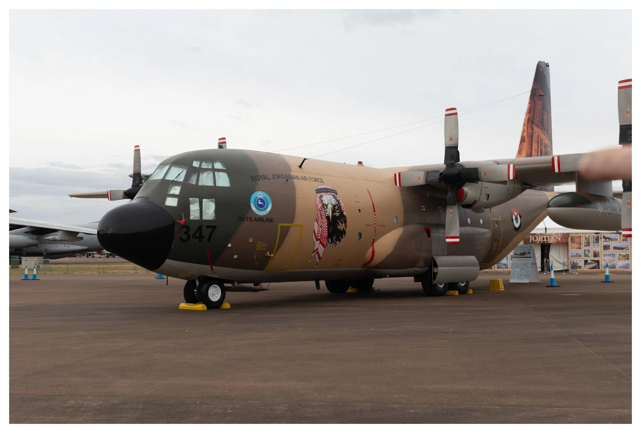 Military aircraft on display at an airshow, painted with desert camouflage and military insignia.