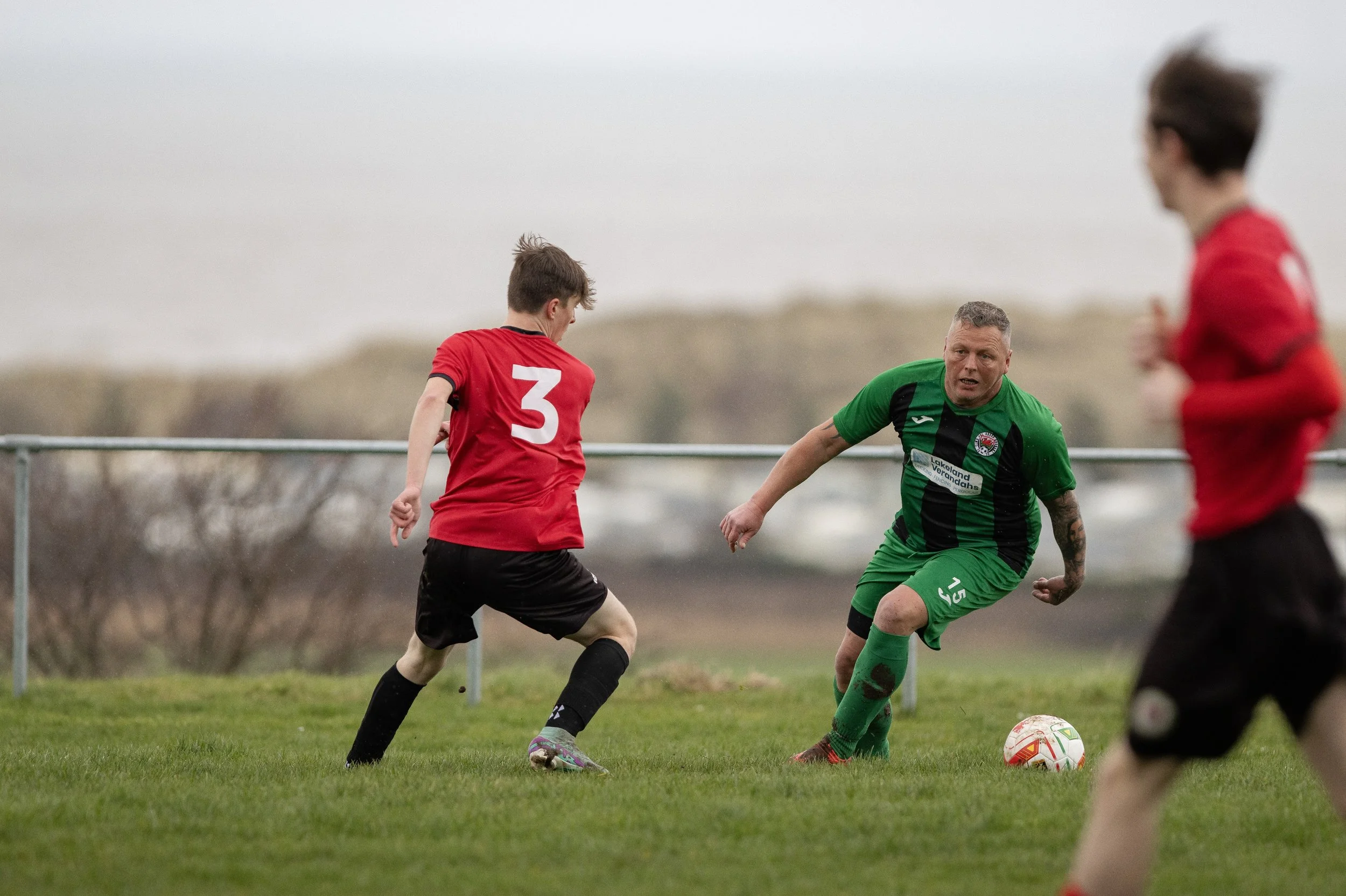 Soccer players competing for the ball on the field during a game, with a view of the landscape in the background.