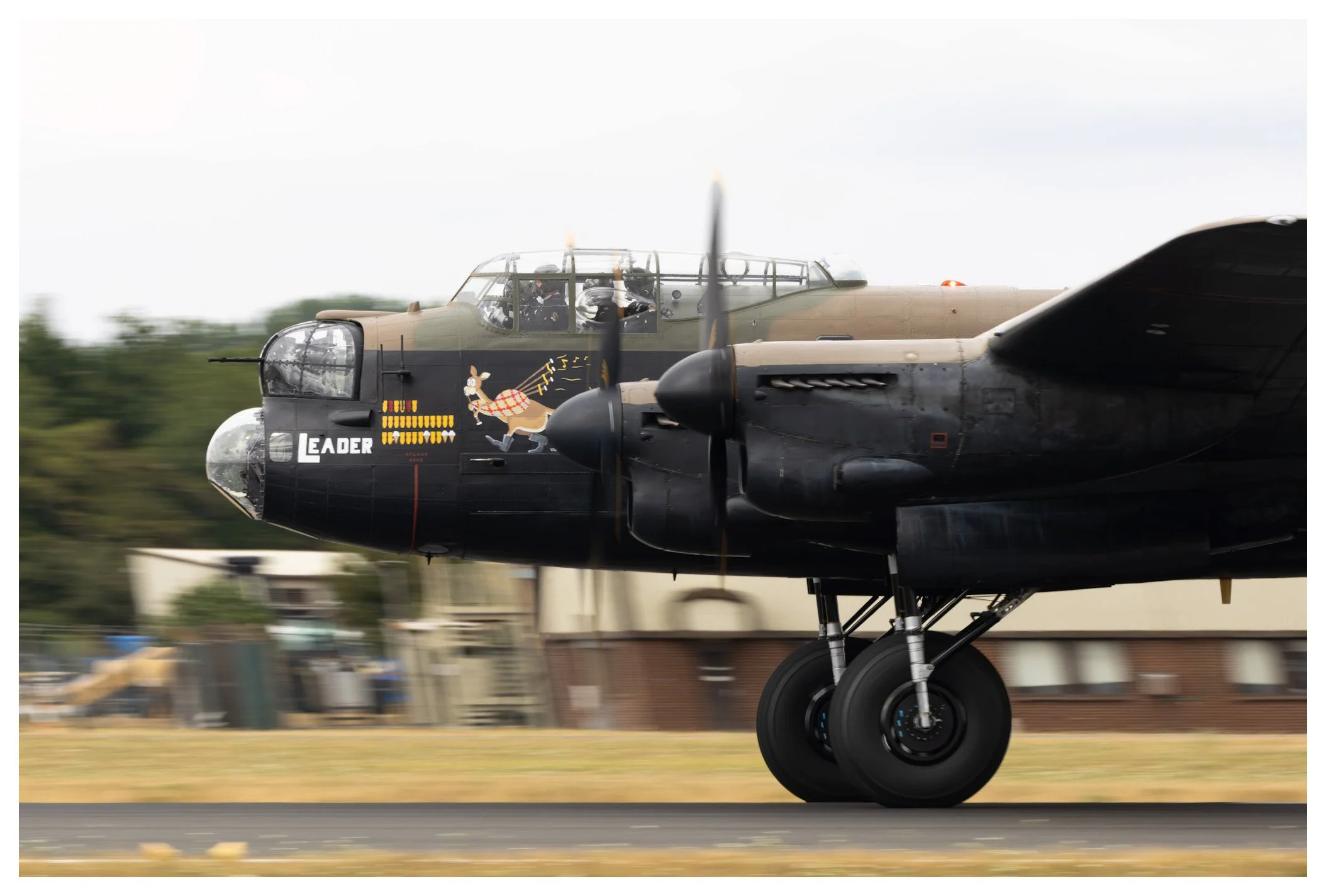 Military aircraft in motion preparing to take off, with a nose art depicting a cartoon deer in a red checkered shirt running, and the word 'LEADER' written on the nose.