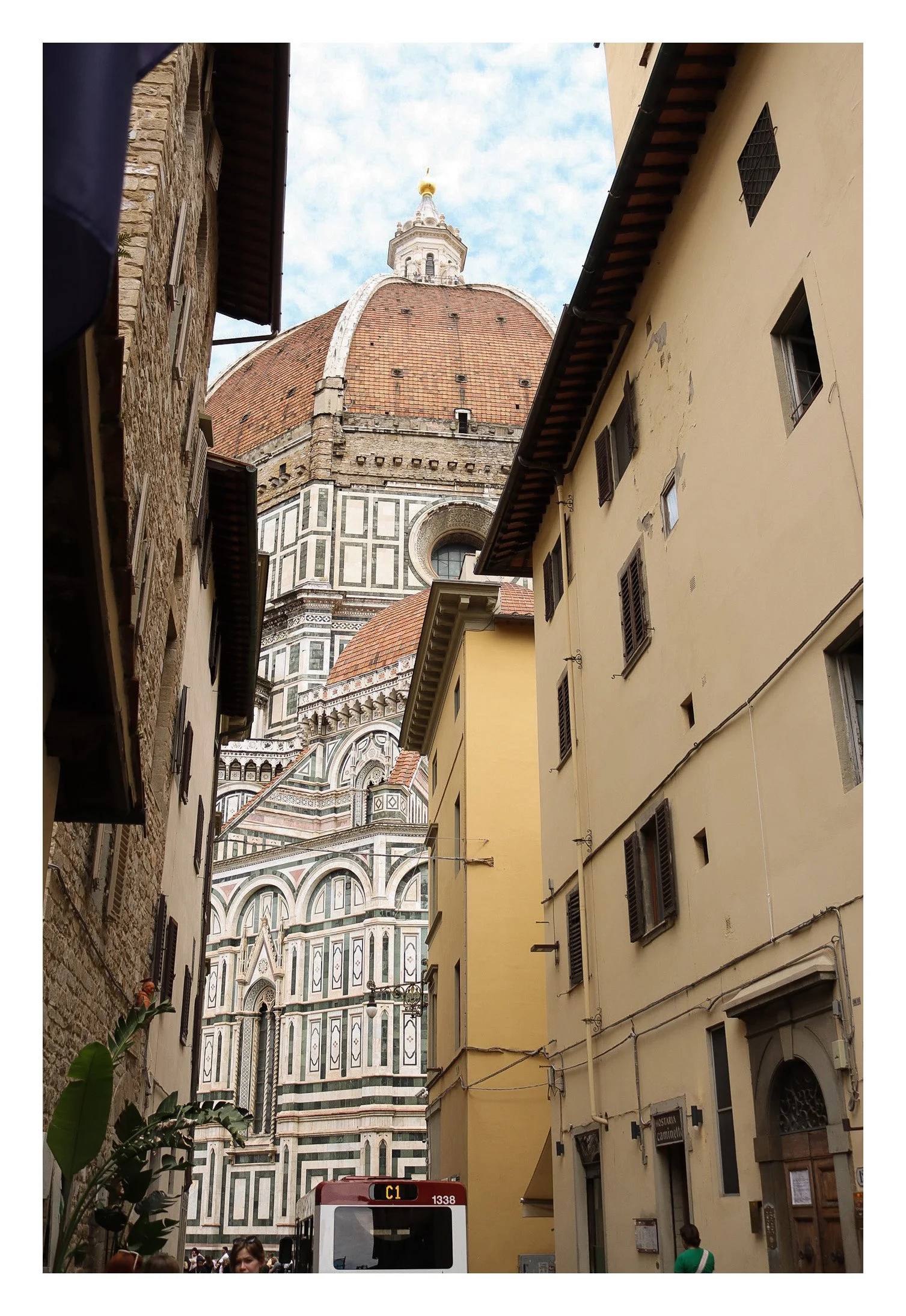 A street view looking up at the Florence Cathedral's dome in Florence, Italy, with surrounding buildings in the foreground and the sky above.