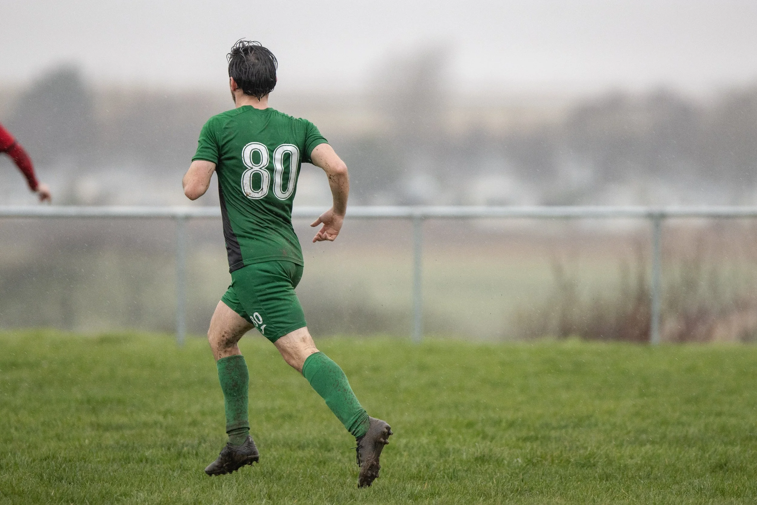 A soccer player wearing a green uniform with the number 80 running on a grassy field in rainy weather.