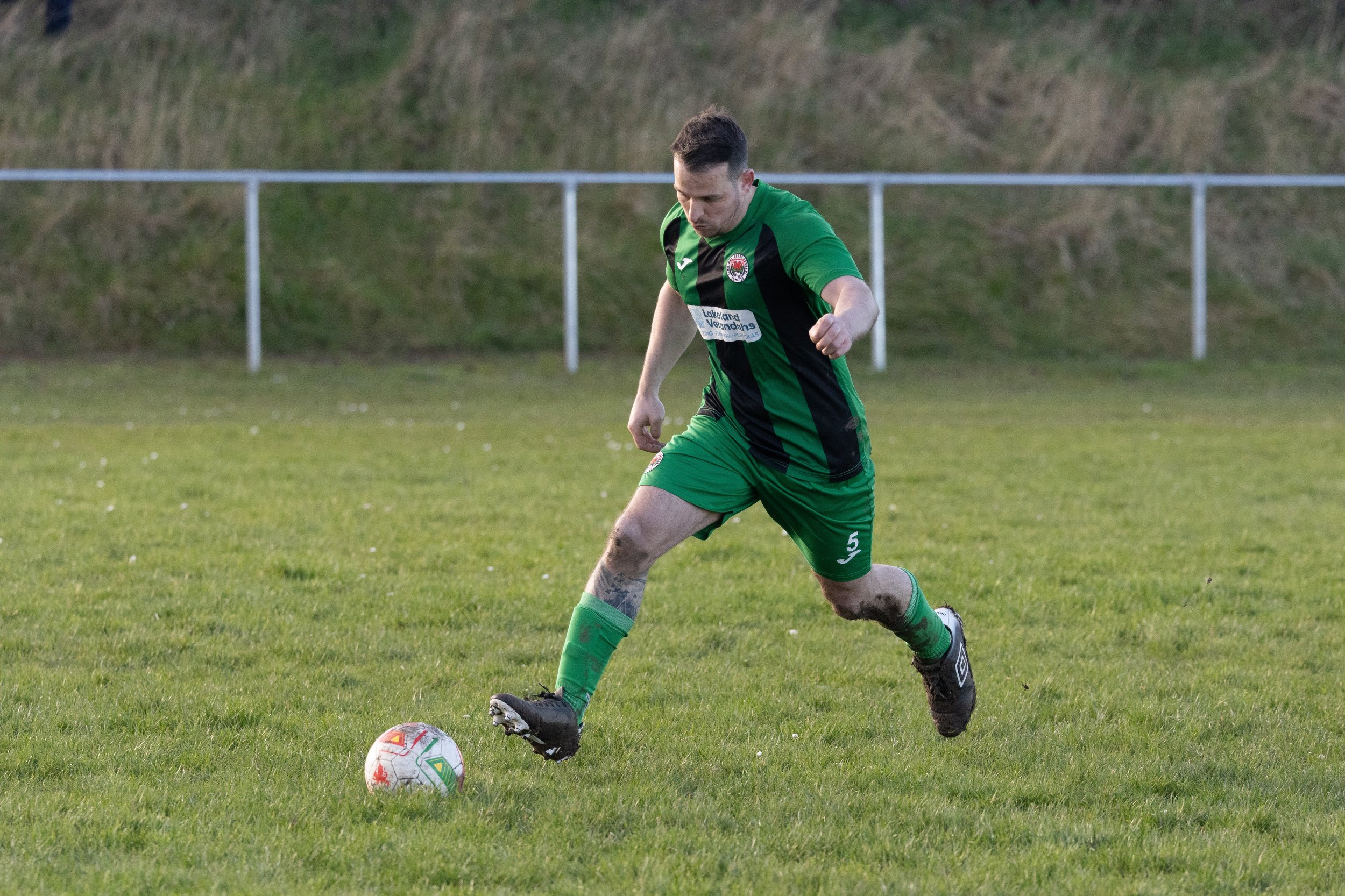 A male soccer player in a green and black uniform kicking a soccer ball on a grassy field.