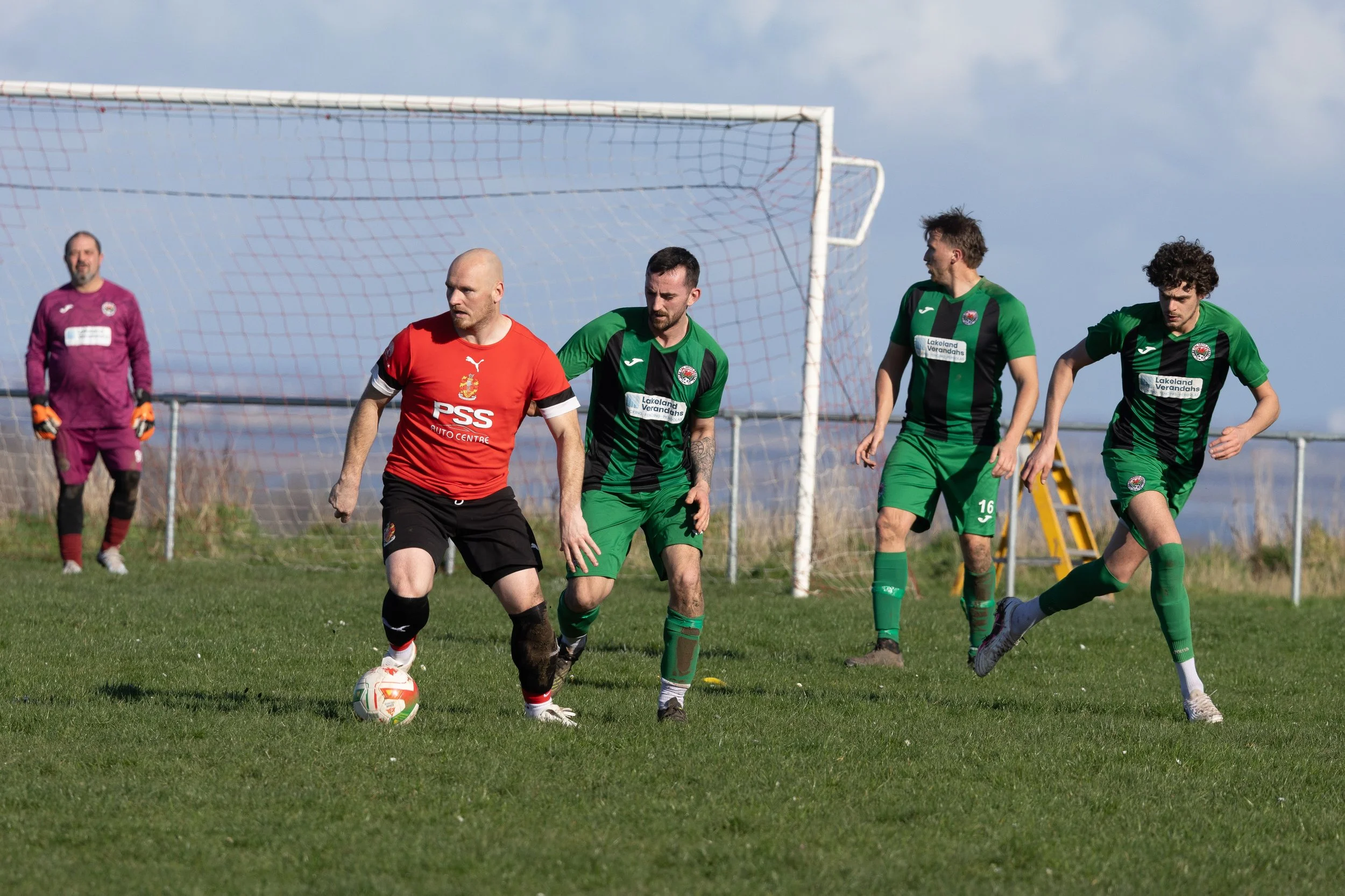 Soccer players on a grassy field competing for the ball with a goalkeeper in the background.