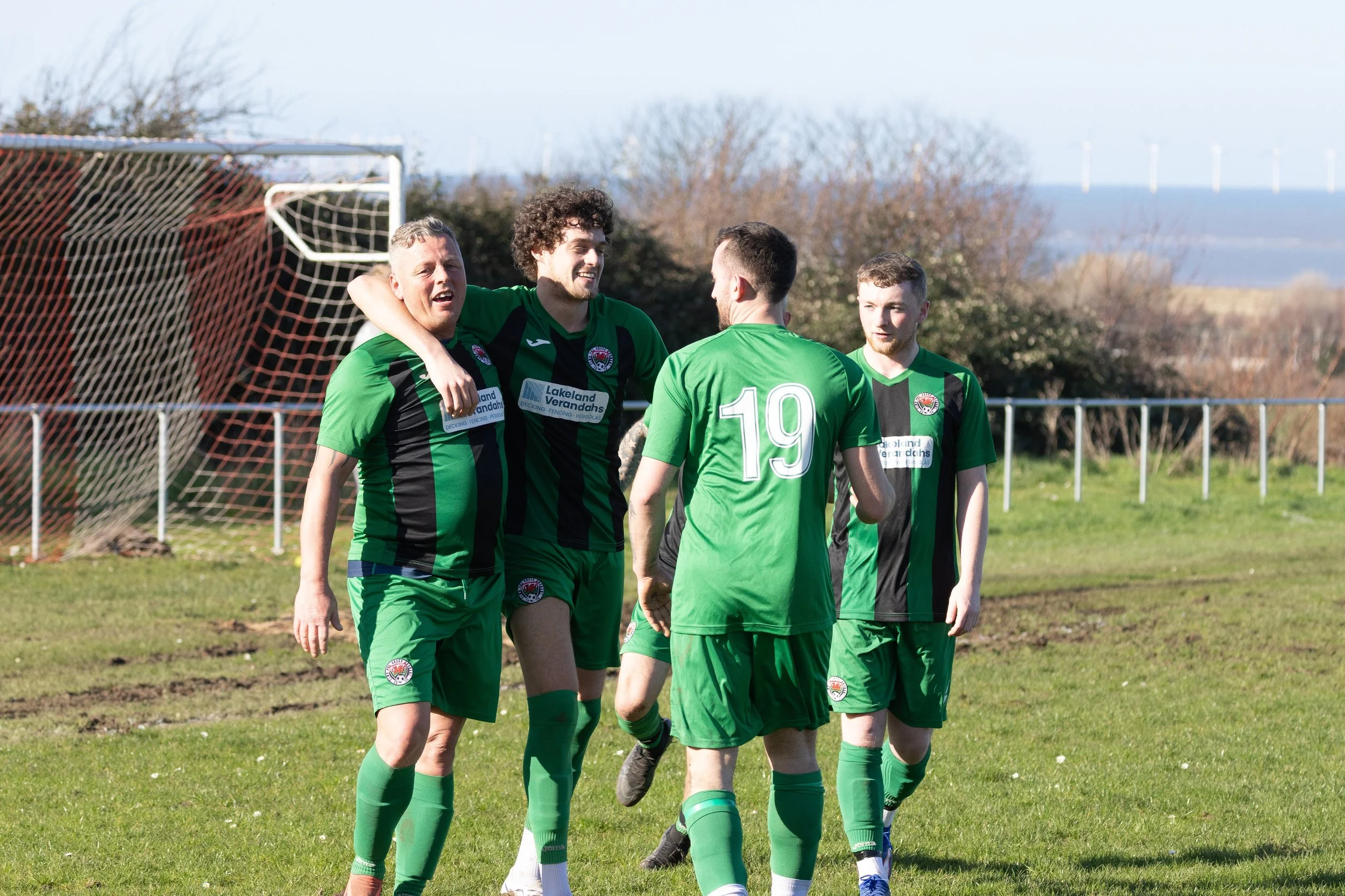 Soccer players in green jerseys celebrating on the field near the goalpost.