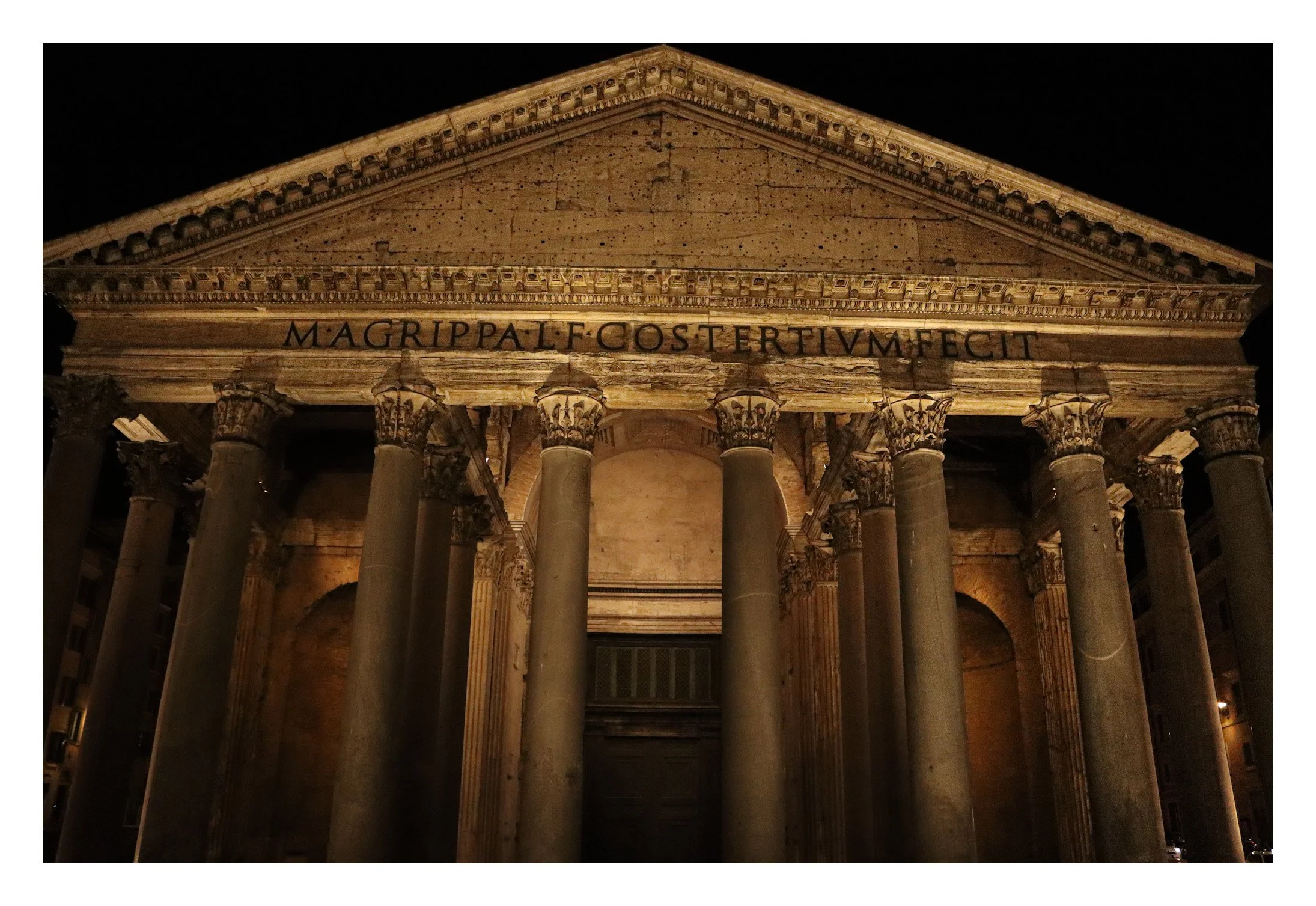 Night view of the ancient Roman Pantheon building with stone columns and triangular pediment, illuminated against the dark sky.