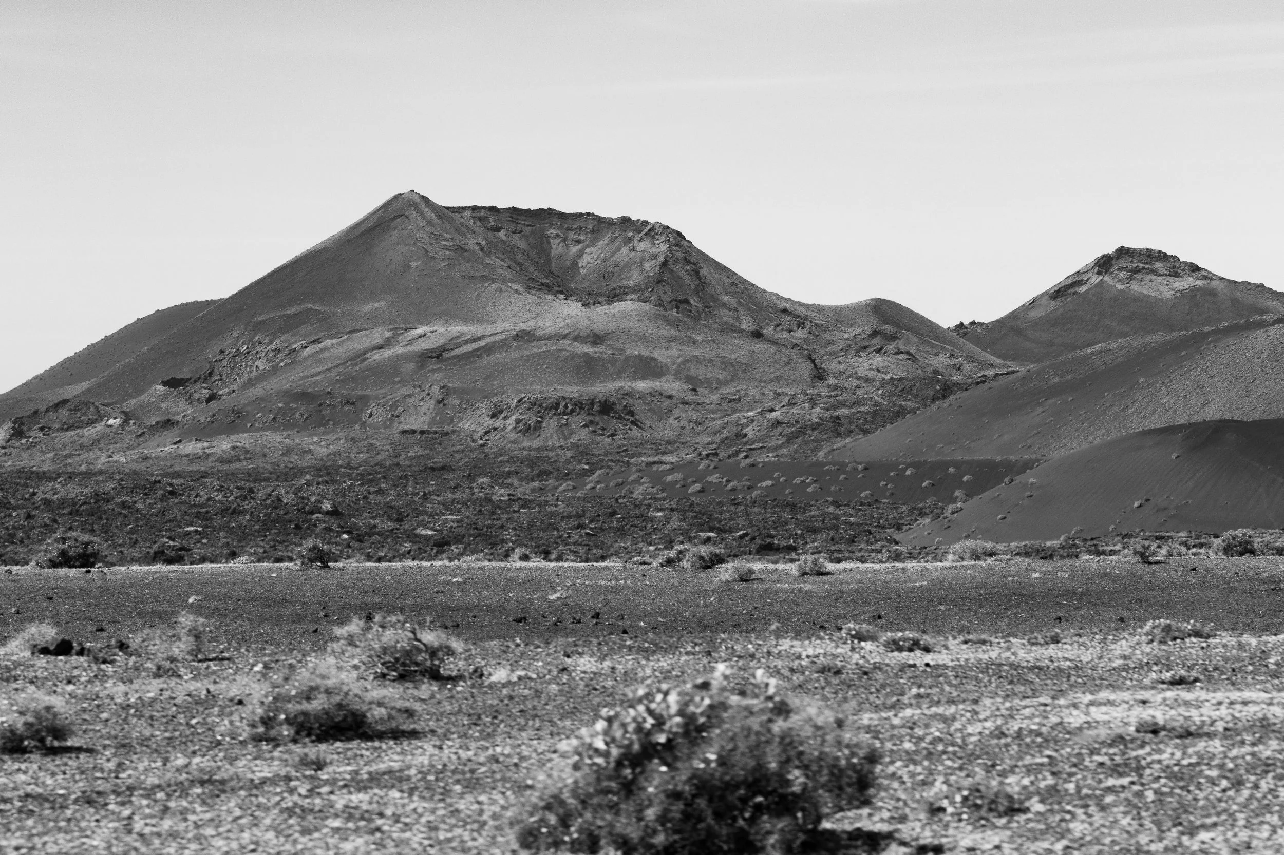 A black and white desert landscape with arid terrain and mountains in the background.