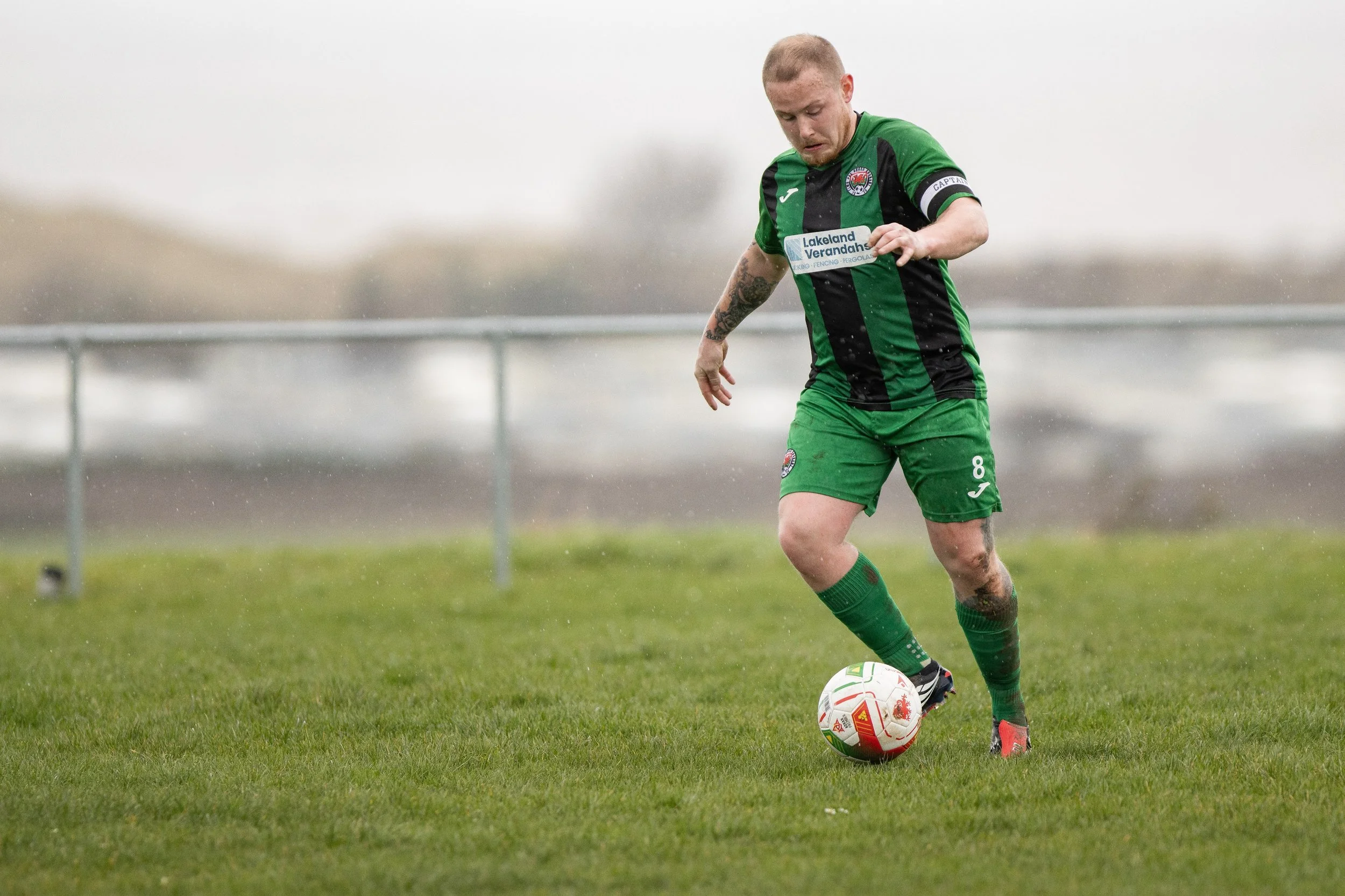 soccer player in green and black uniform kicking a soccer ball on a grassy field
