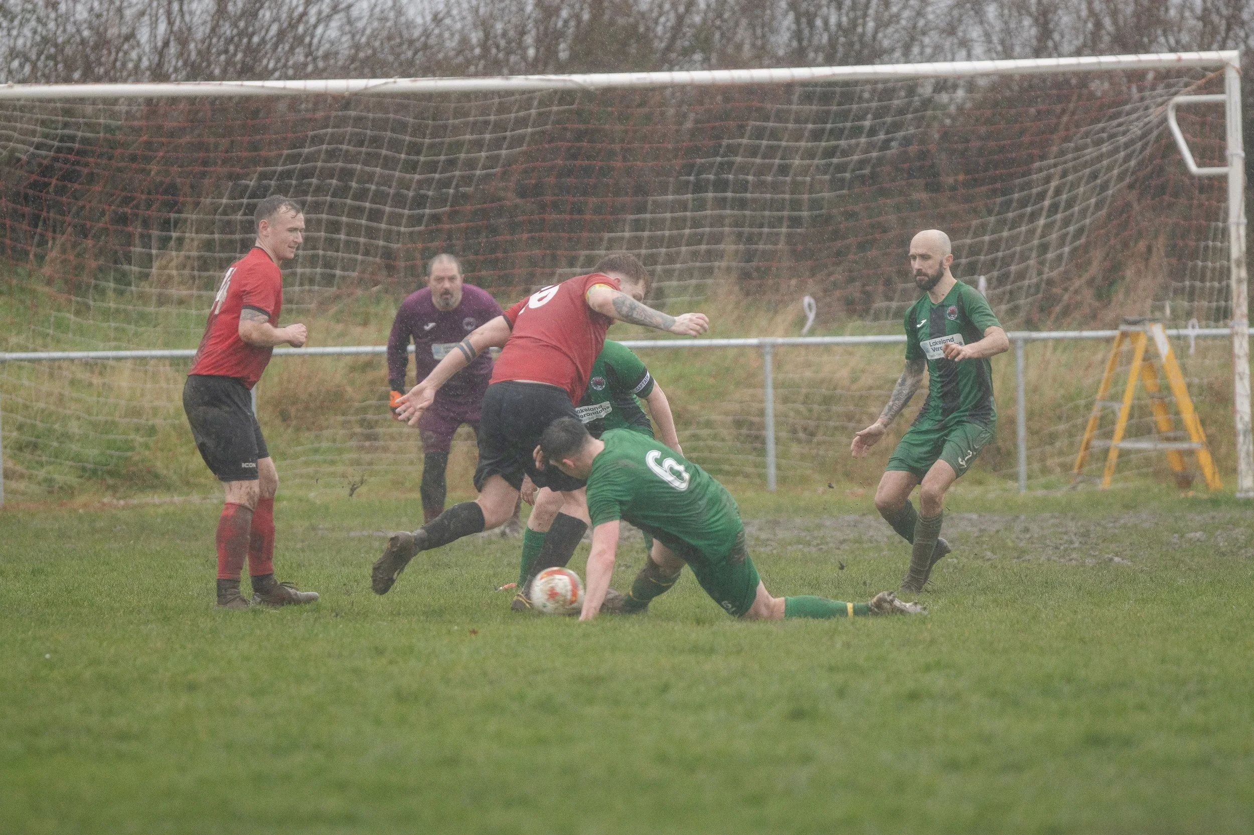 A soccer match in rain with players fighting for the ball near the goal; some players are muddy and wet.