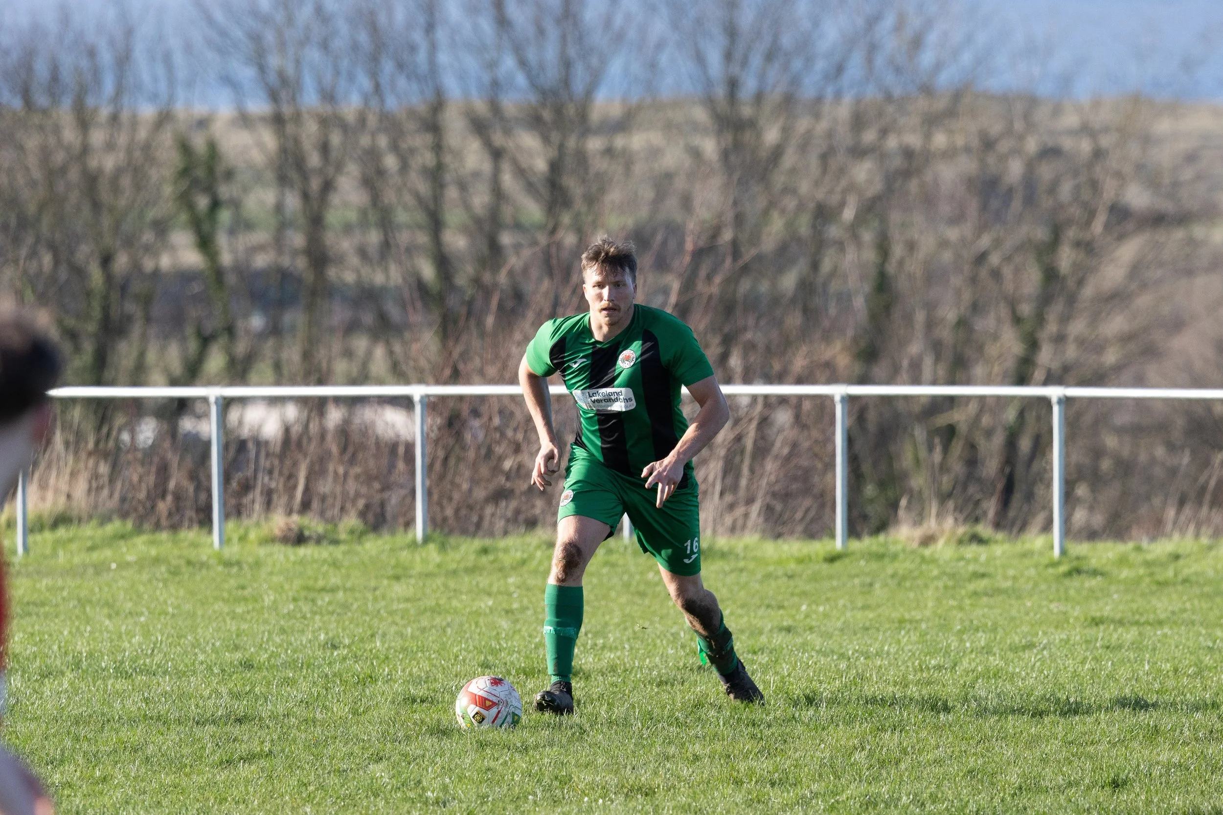 A soccer player in a green uniform on a field, preparing to kick a soccer ball.