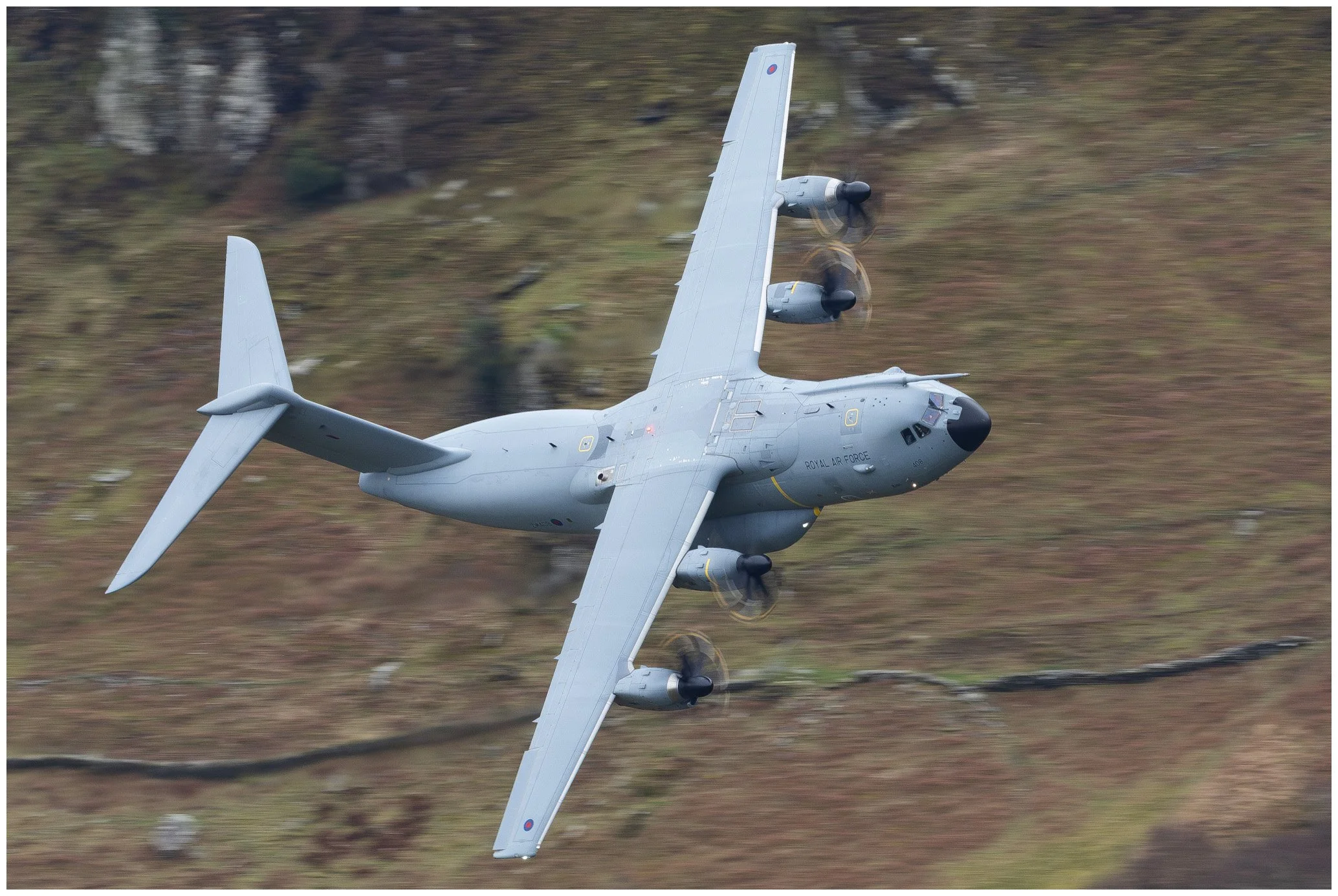 A military aircraft flying low over a mountainous terrain.