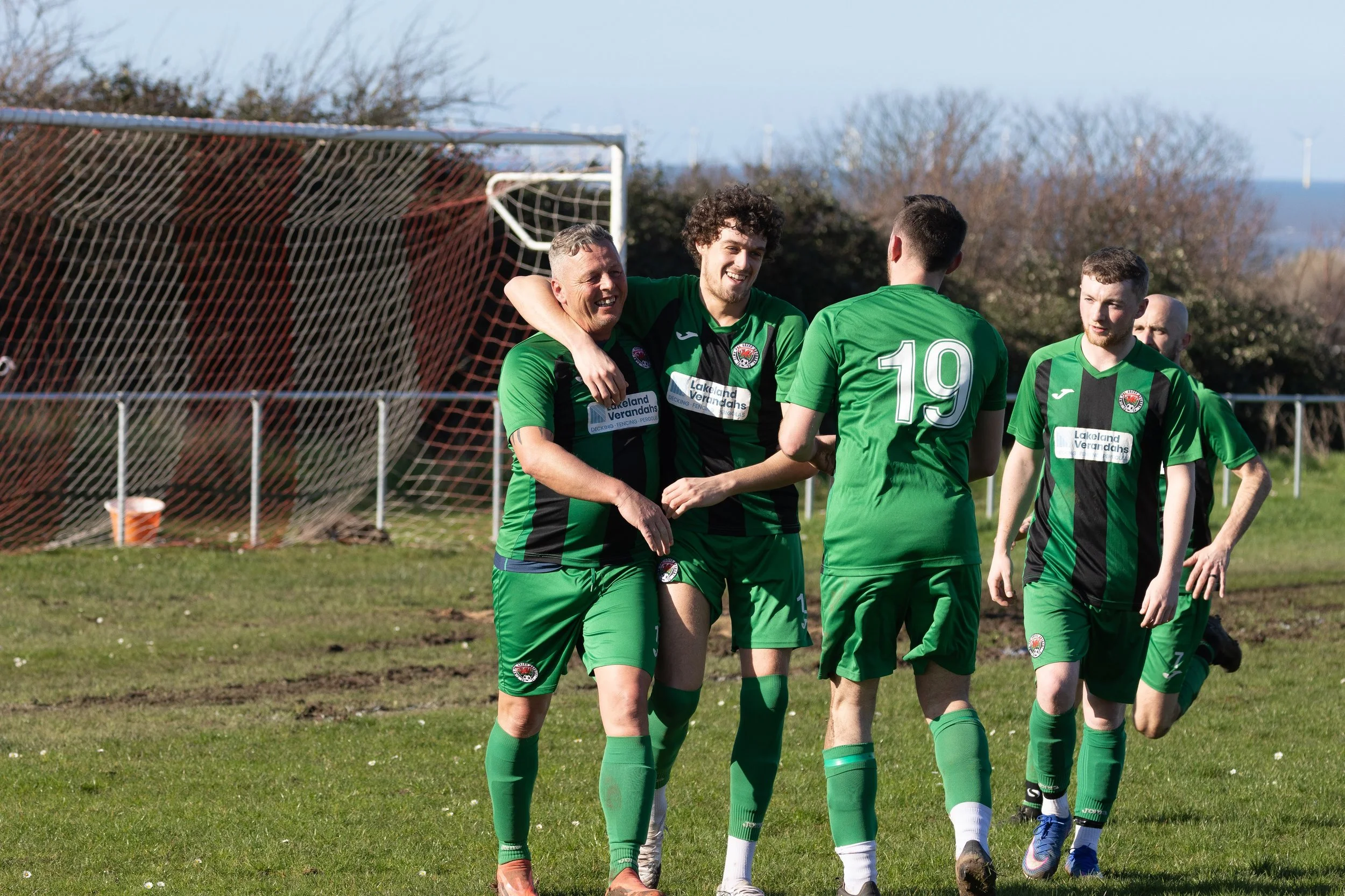 Group of soccer players in green and black uniforms celebrating on the field