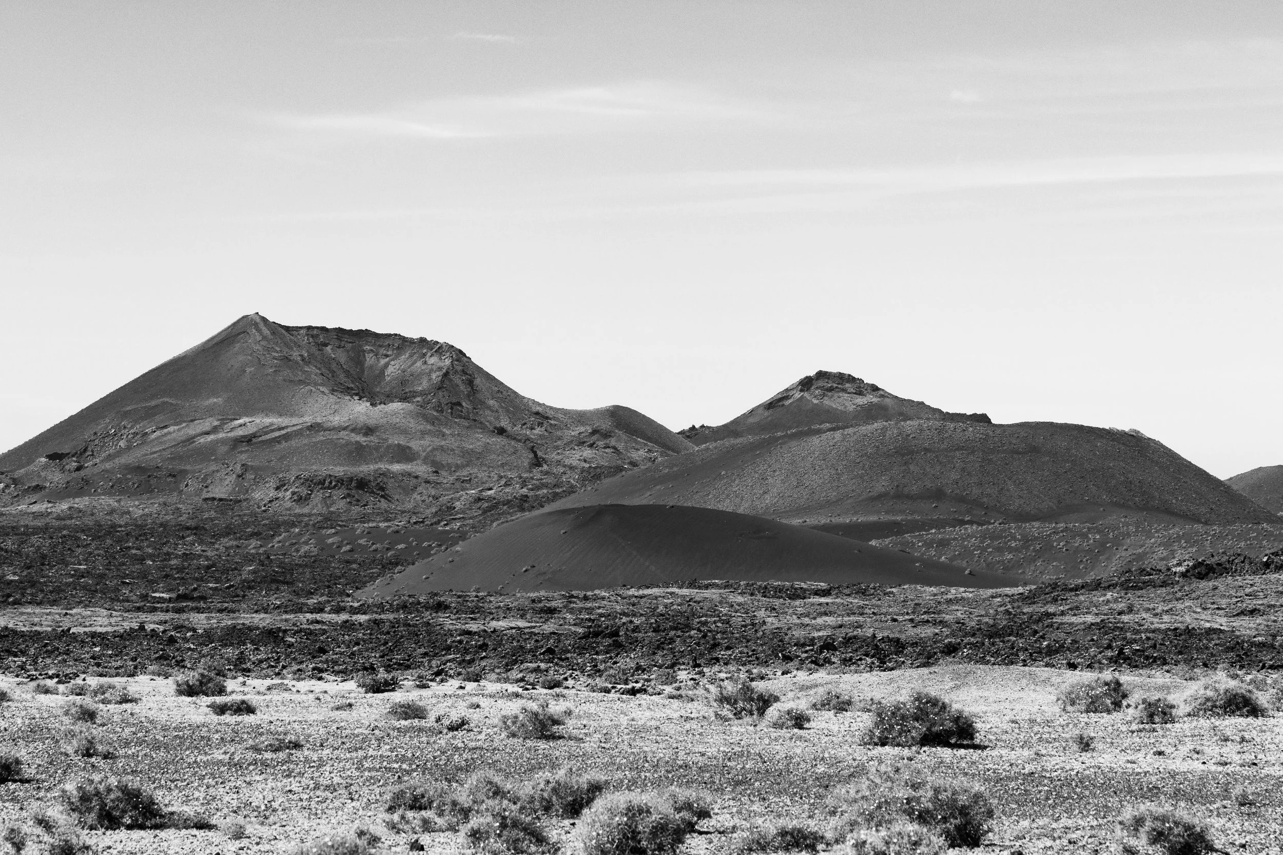 Black and white photo of volcanic mountains in a desert landscape, with barren rocky ground and sparse vegetation.