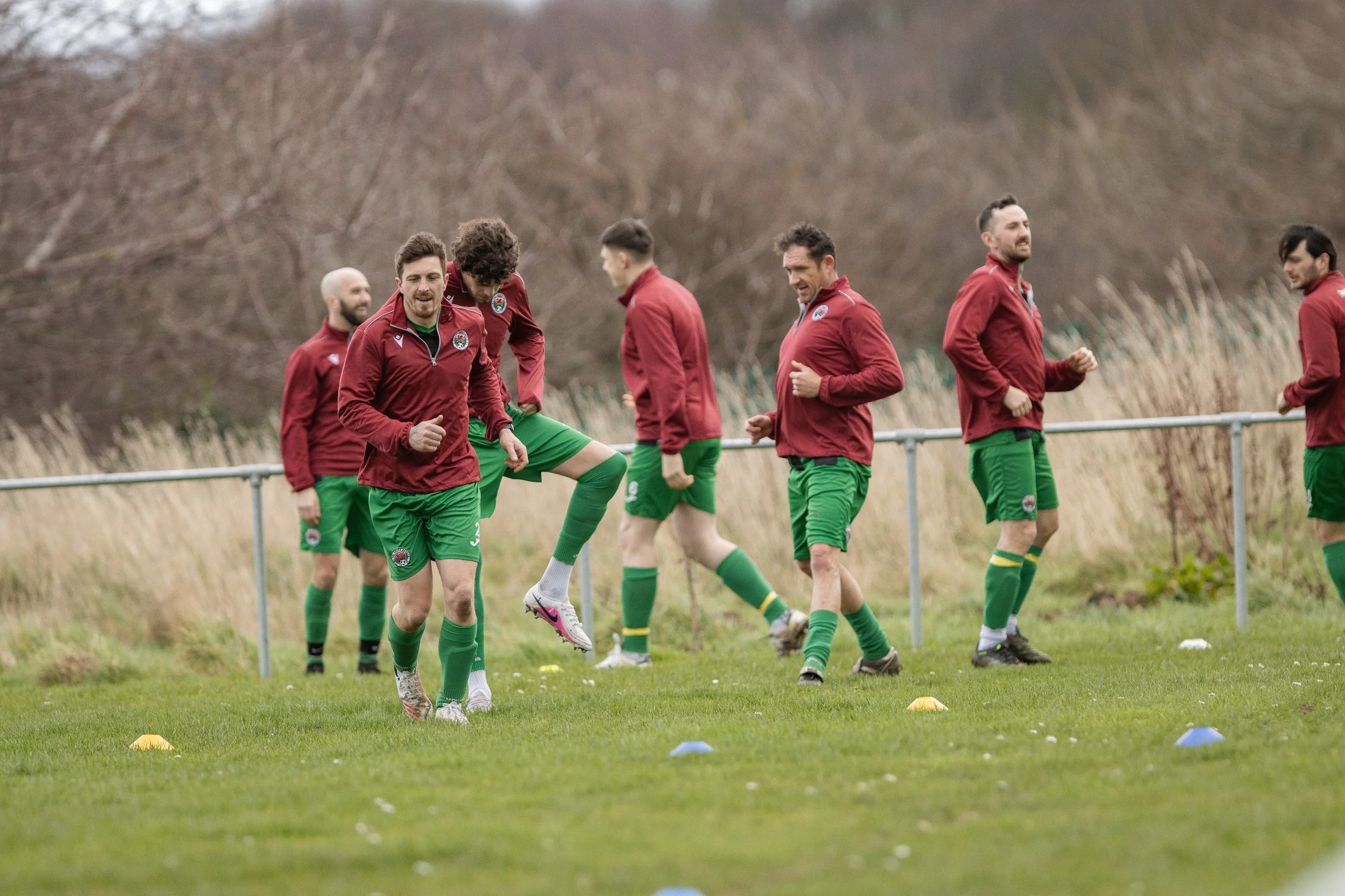 Group of male soccer players in red jackets and green shorts training on a grassy field.