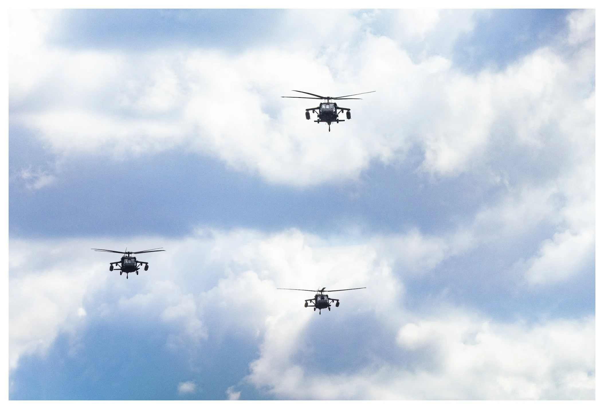 Three military helicopters flying in formation against a partly cloudy sky.