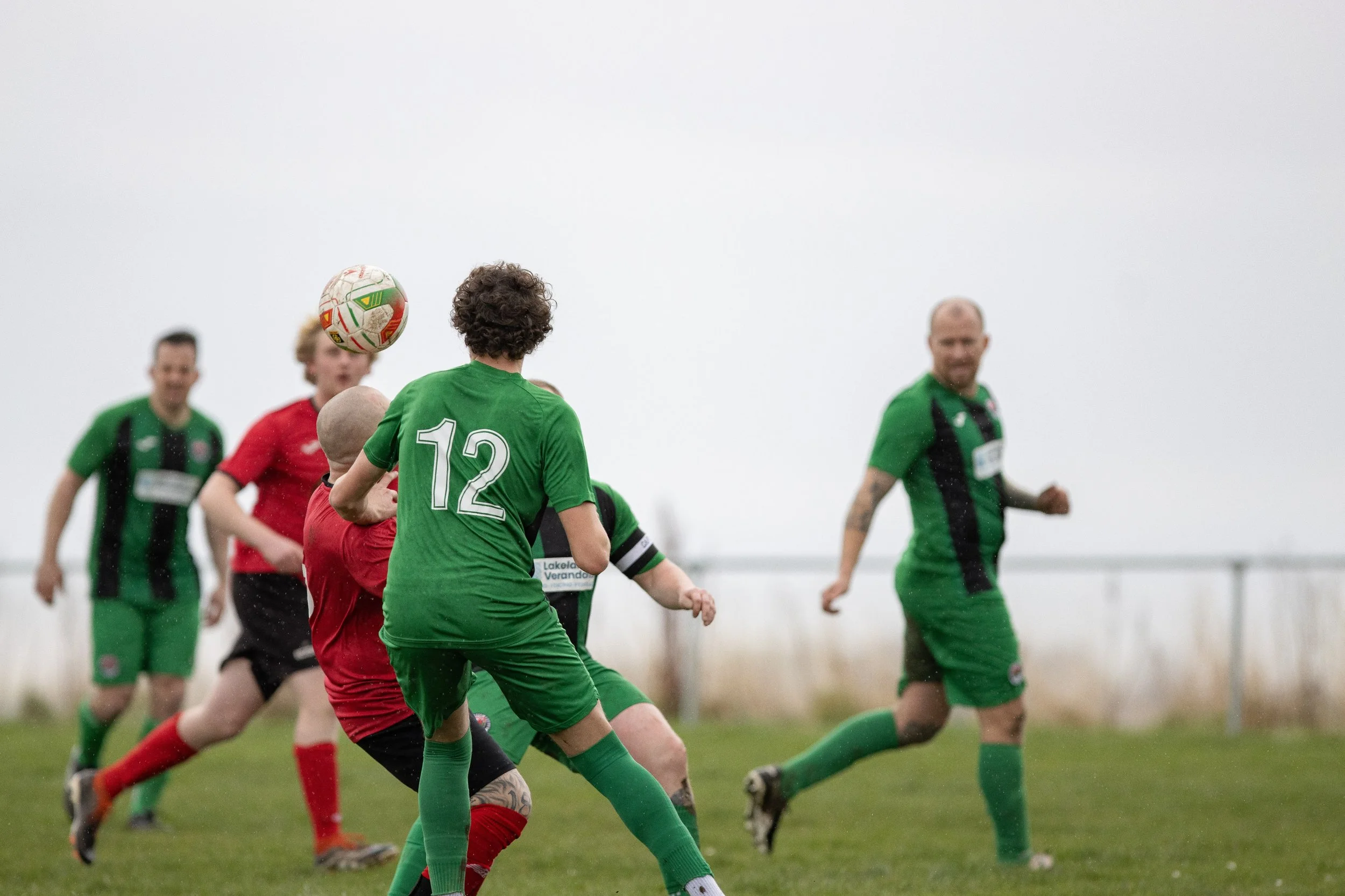 Soccer players in green and red uniforms playing on a grassy field, focusing on a ball in mid-air.