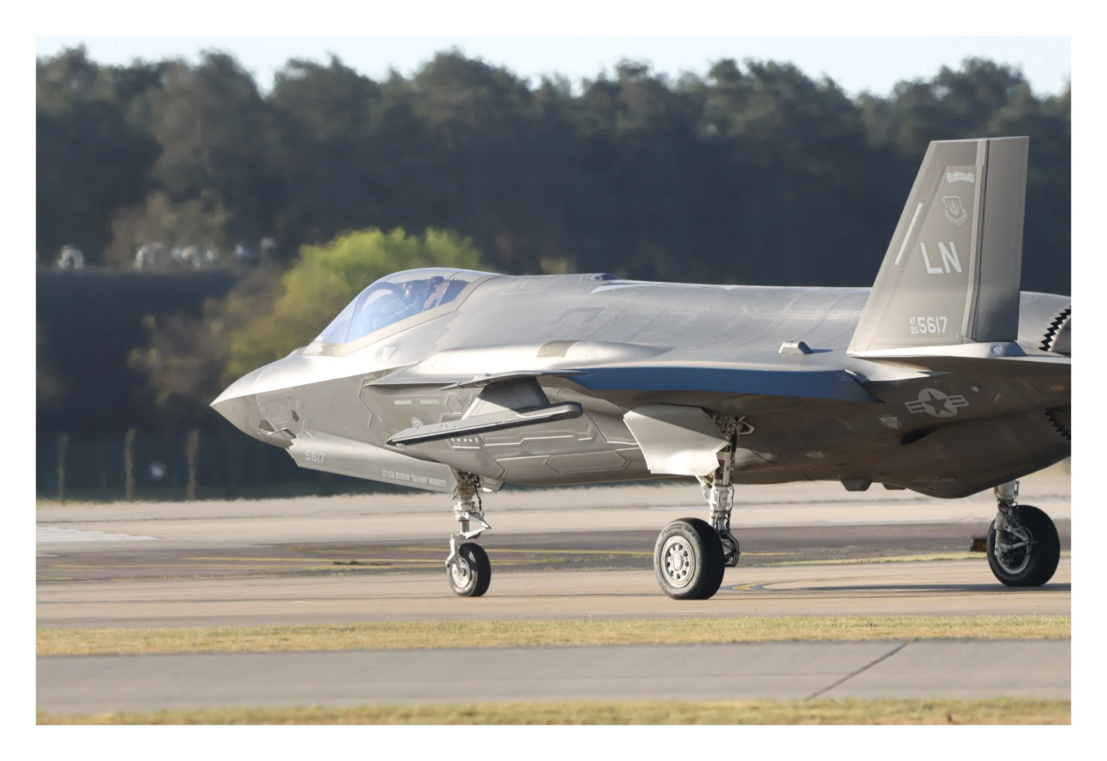 A gray military fighter jet parked on an airstrip with trees in the background.