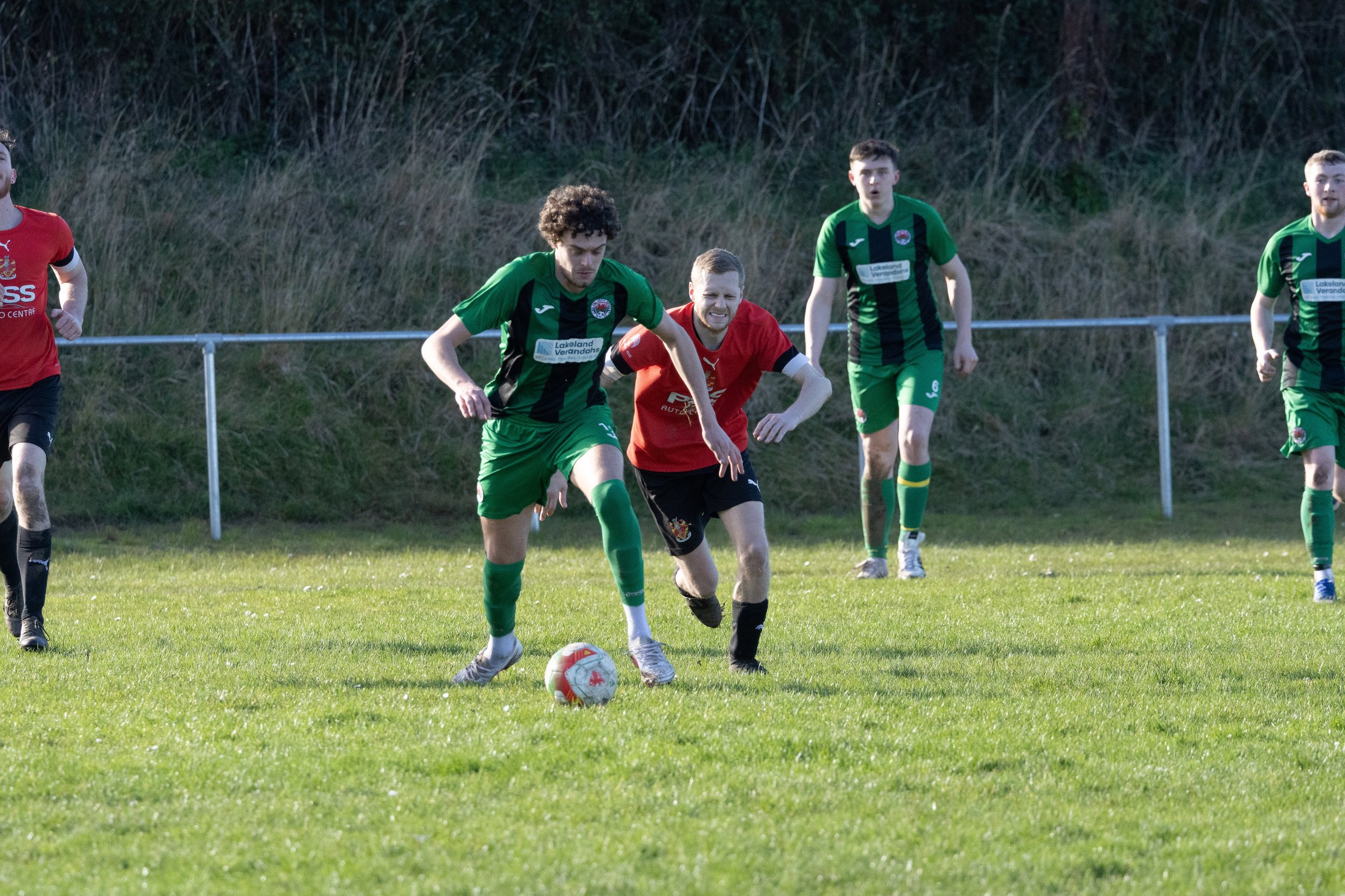 Soccer players in green and black jerseys and red and black jerseys playing on a grassy field during a match.