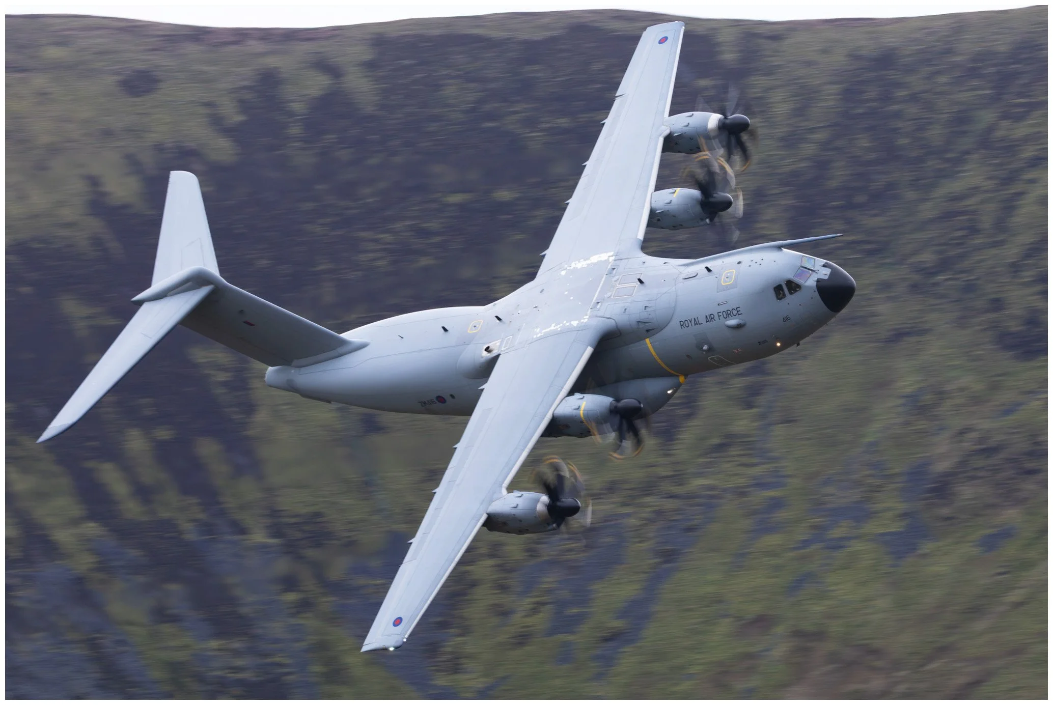 A Royal Air Force aircraft flying low over a mountainous landscape.