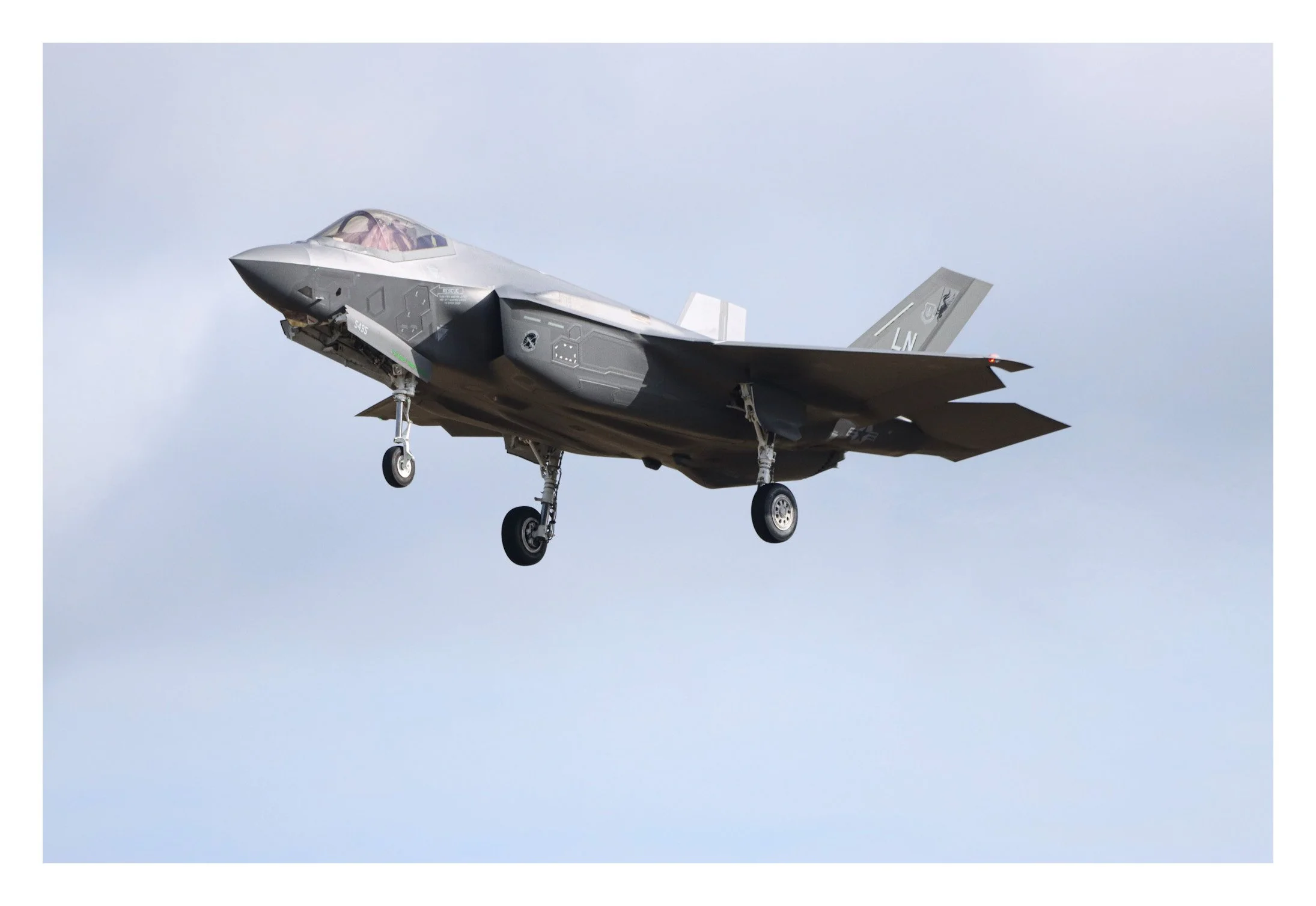 F-35 fighter jet flying against a cloudy sky with landing gear extended.