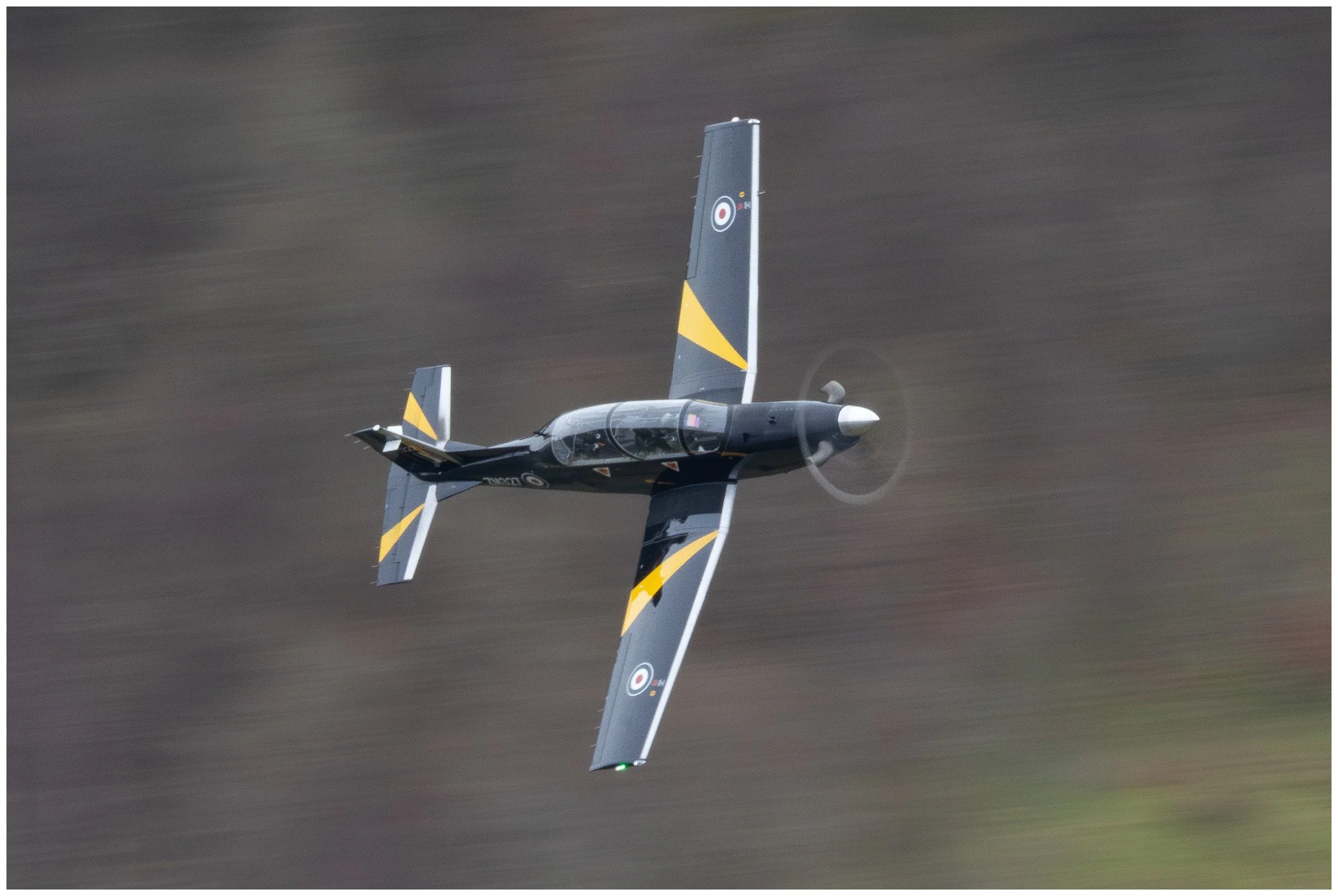 A black and yellow single-engine propeller airplane flying at an angle with a blurred landscape background.
