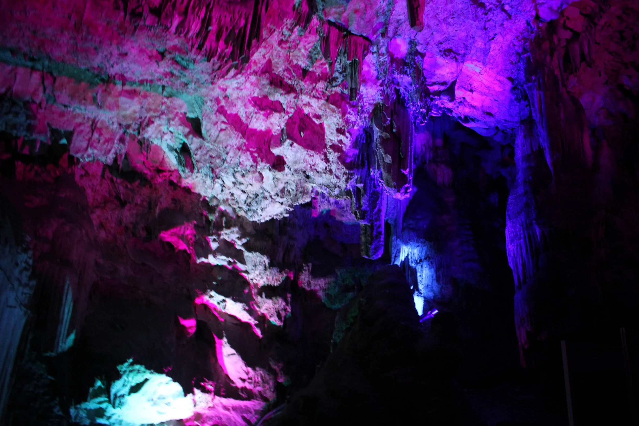Colorful cave formations illuminated by pink, purple, blue, and white lights.