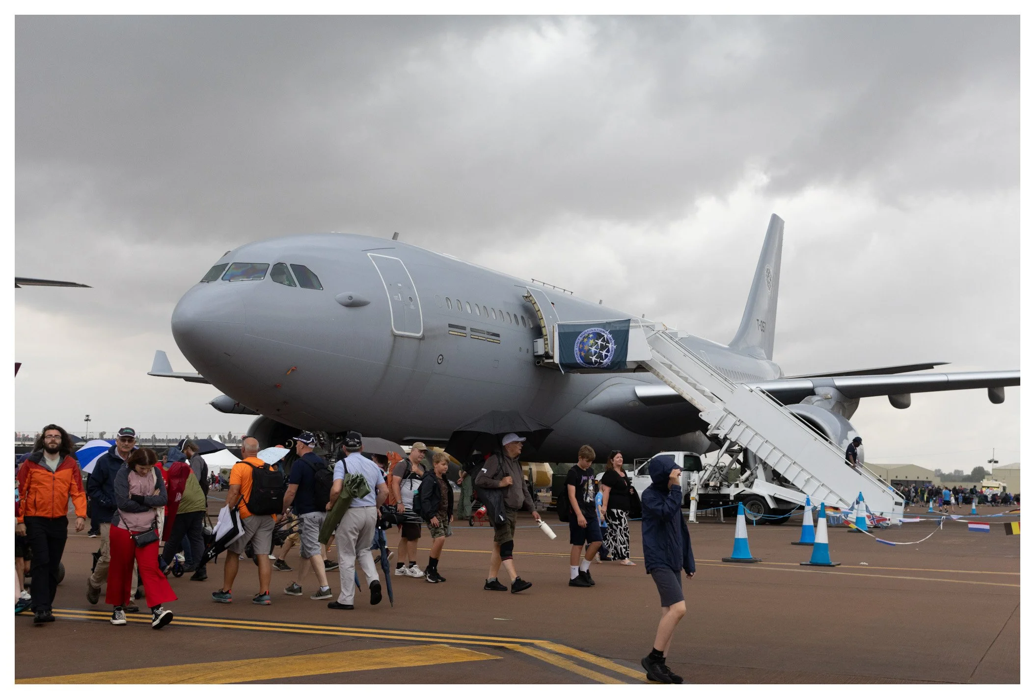 A large aircraft on display at an airshow, with people walking around and looking at it, some using umbrellas due to cloudy weather.