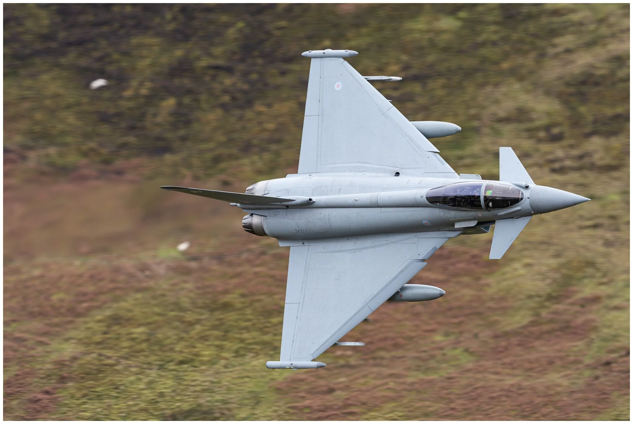 A fighter jet flying low over a grassy terrain, captured from a side angle.