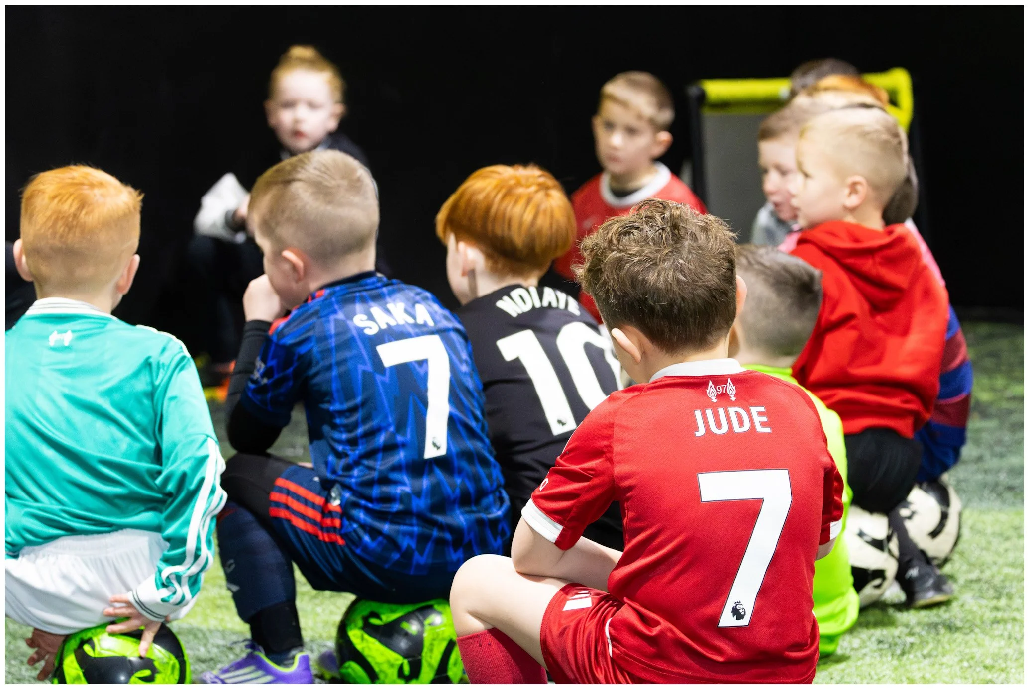 Children sitting on the ground with soccer balls, wearing sports jerseys