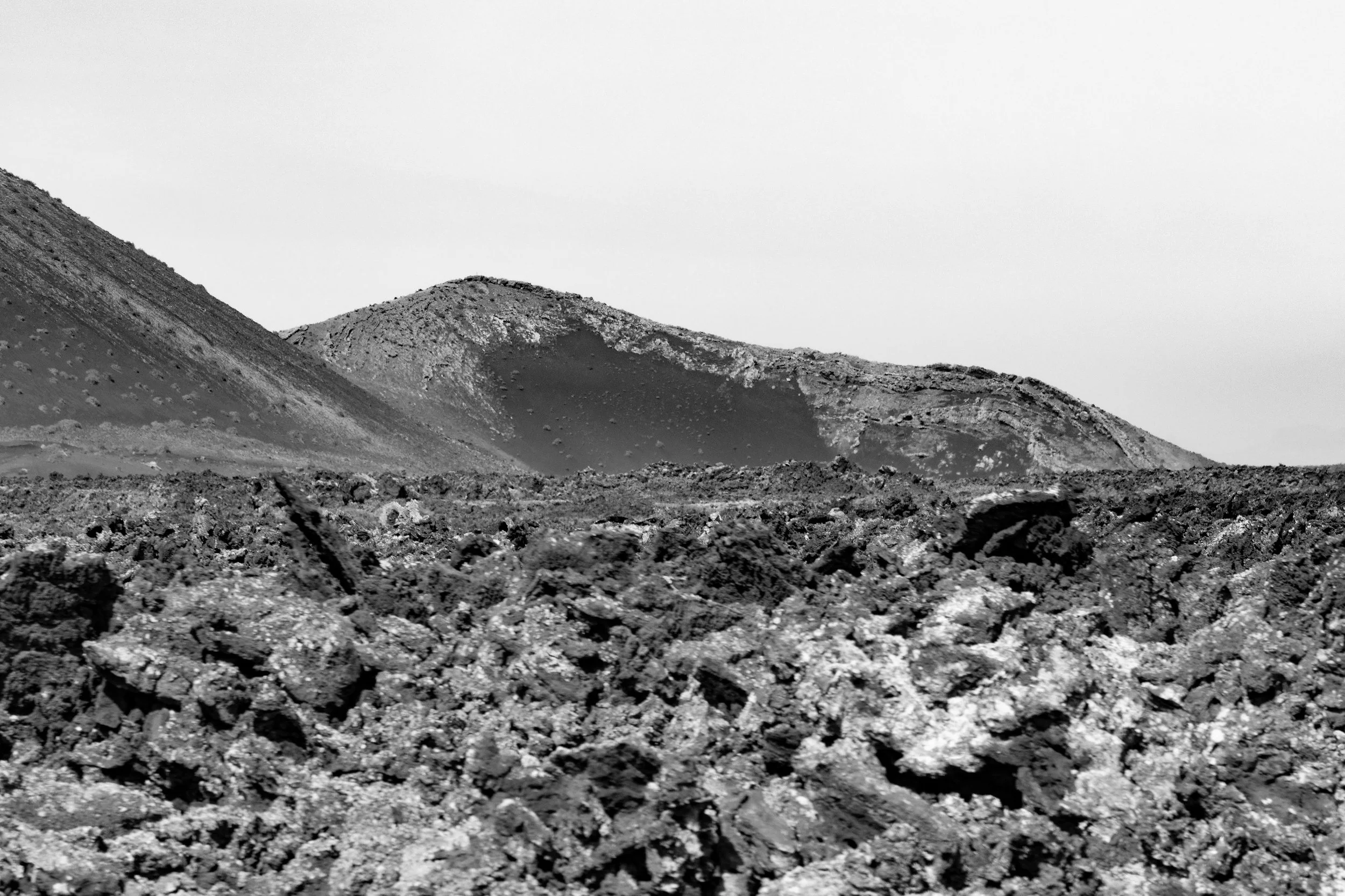 Black and white photo of rugged, rocky terrain with volcanic hills in the background.